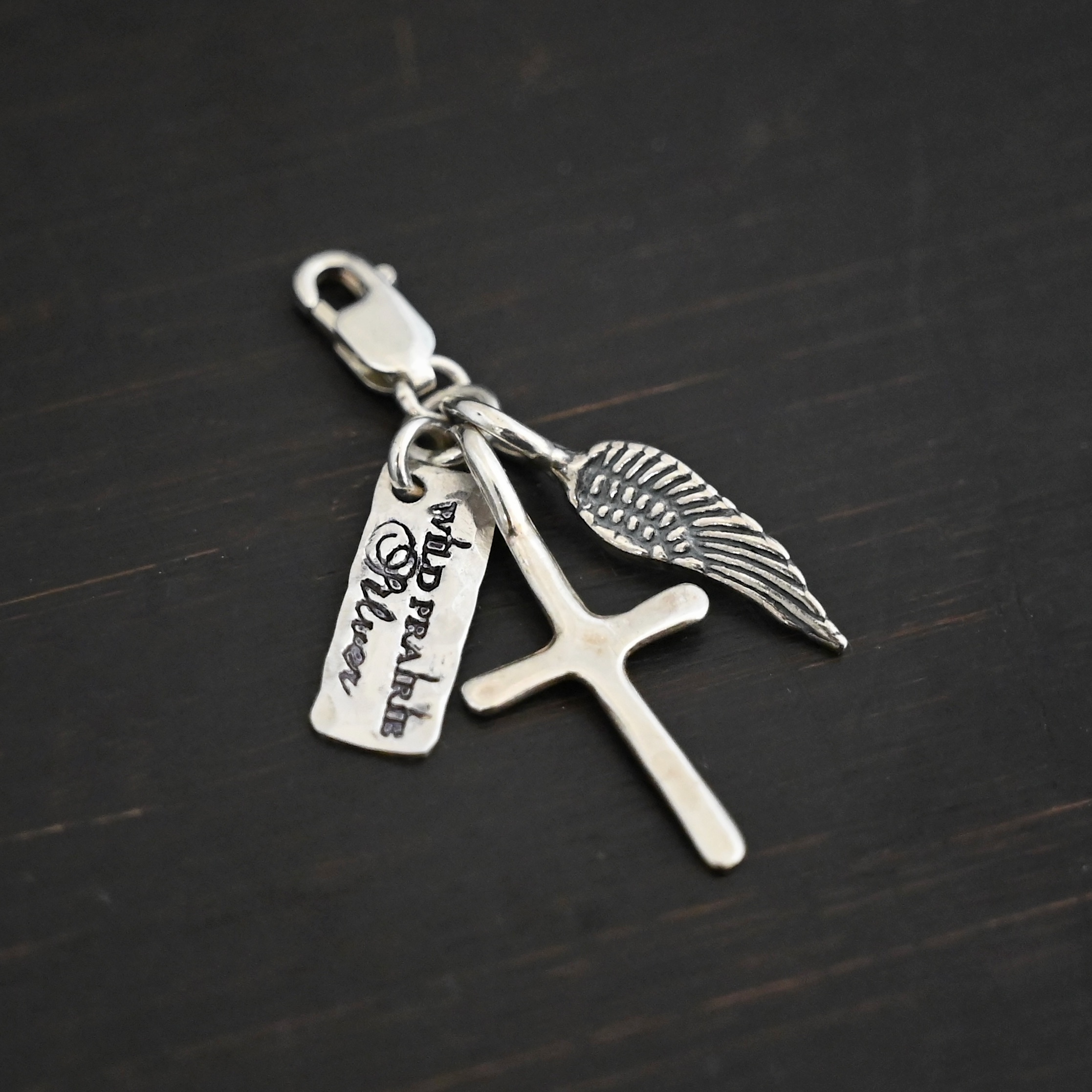 Wild Prairie Charm - shiny shown on dark background - wild prairie tag, cross & angel wing charm