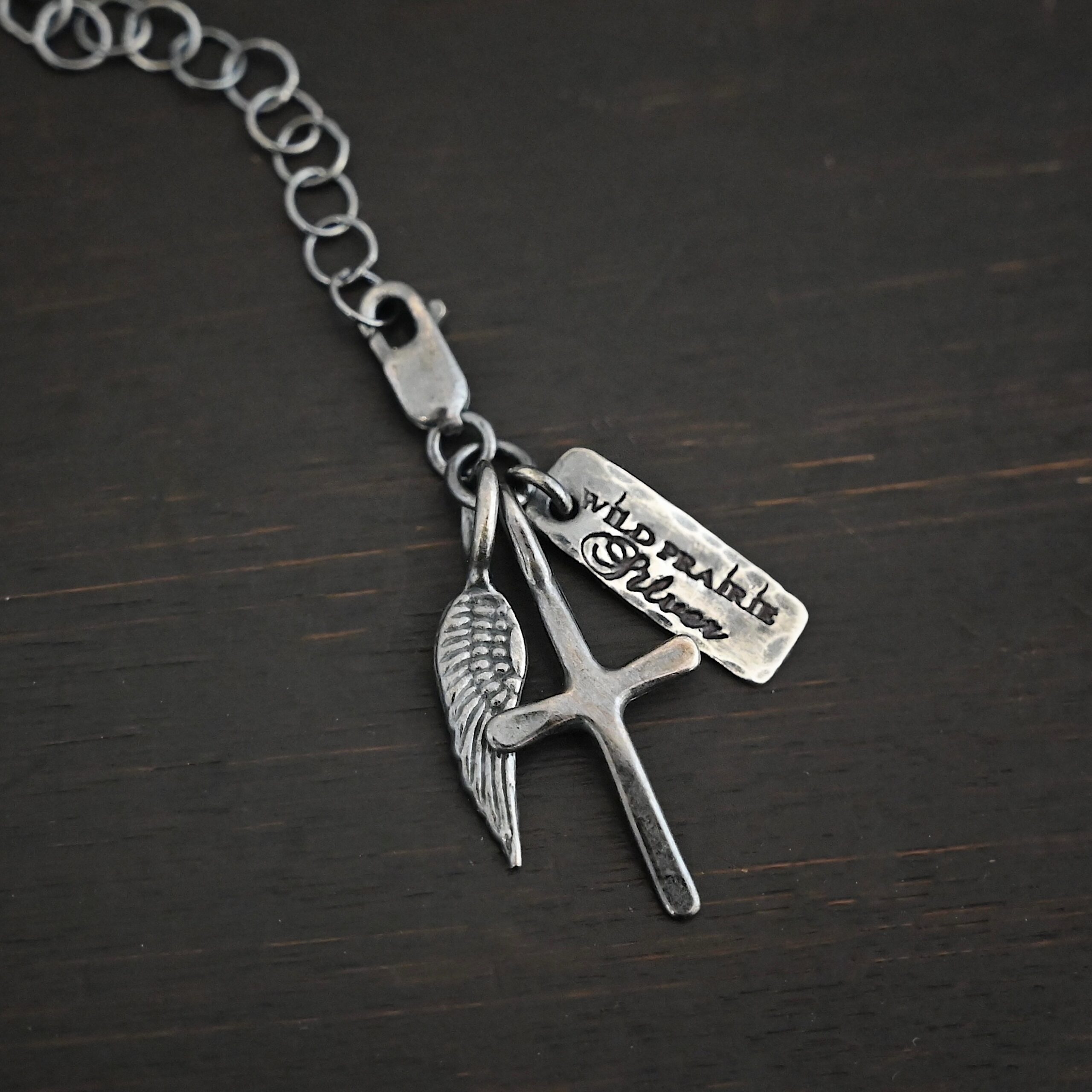 Wild Prairie Charm - oxidized shown on dark background - wild prairie tag, cross & angel wing charm