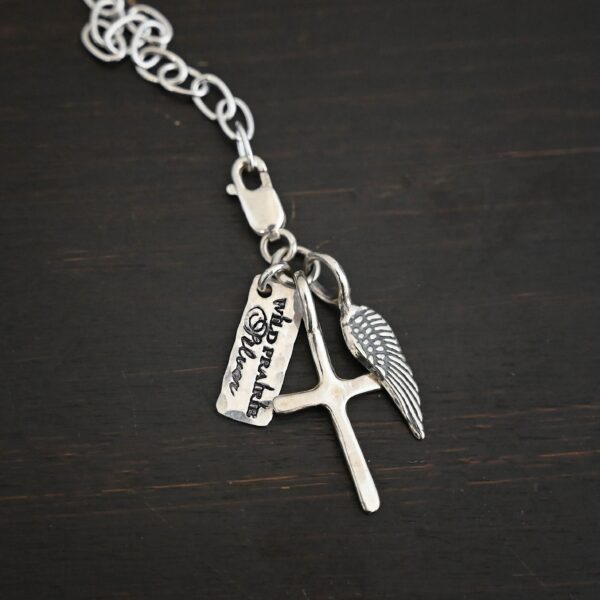 Wild Prairie Charm - shiny shown on dark background - wild prairie tag, cross & angel wing charm