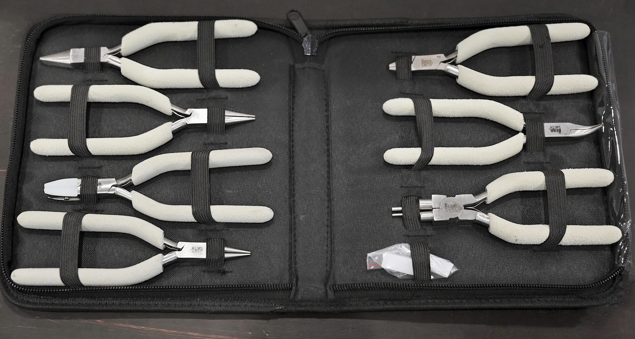 Shows entire set of tools in its tool bag - 7 pliers total with white foam handles in black nylon bag