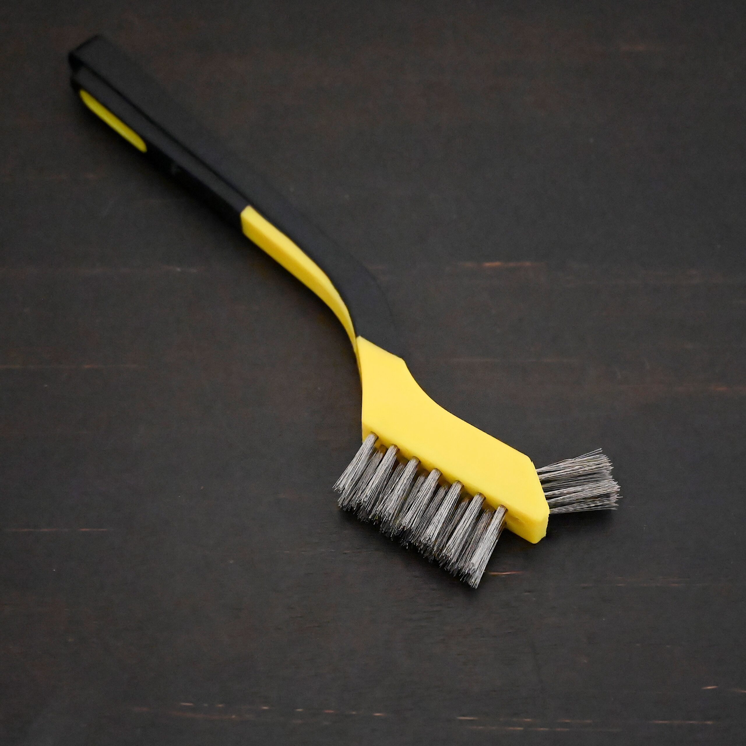 Stainless Steel Wire Brush - black and yellow plastic handle shown on dark background
