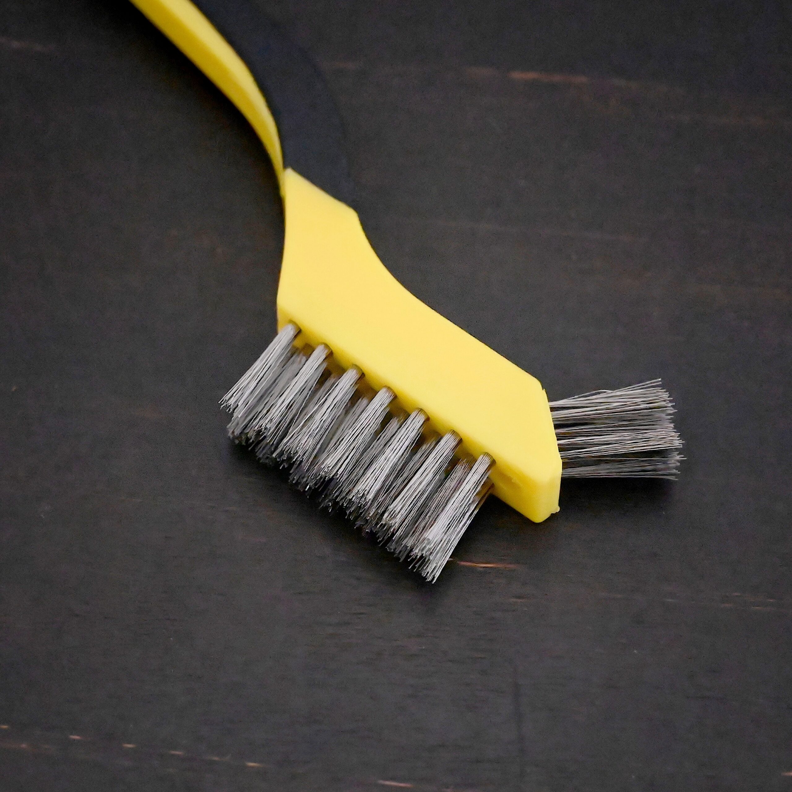 Stainless Steel Wire Brush - black and yellow plastic handle shown on dark background