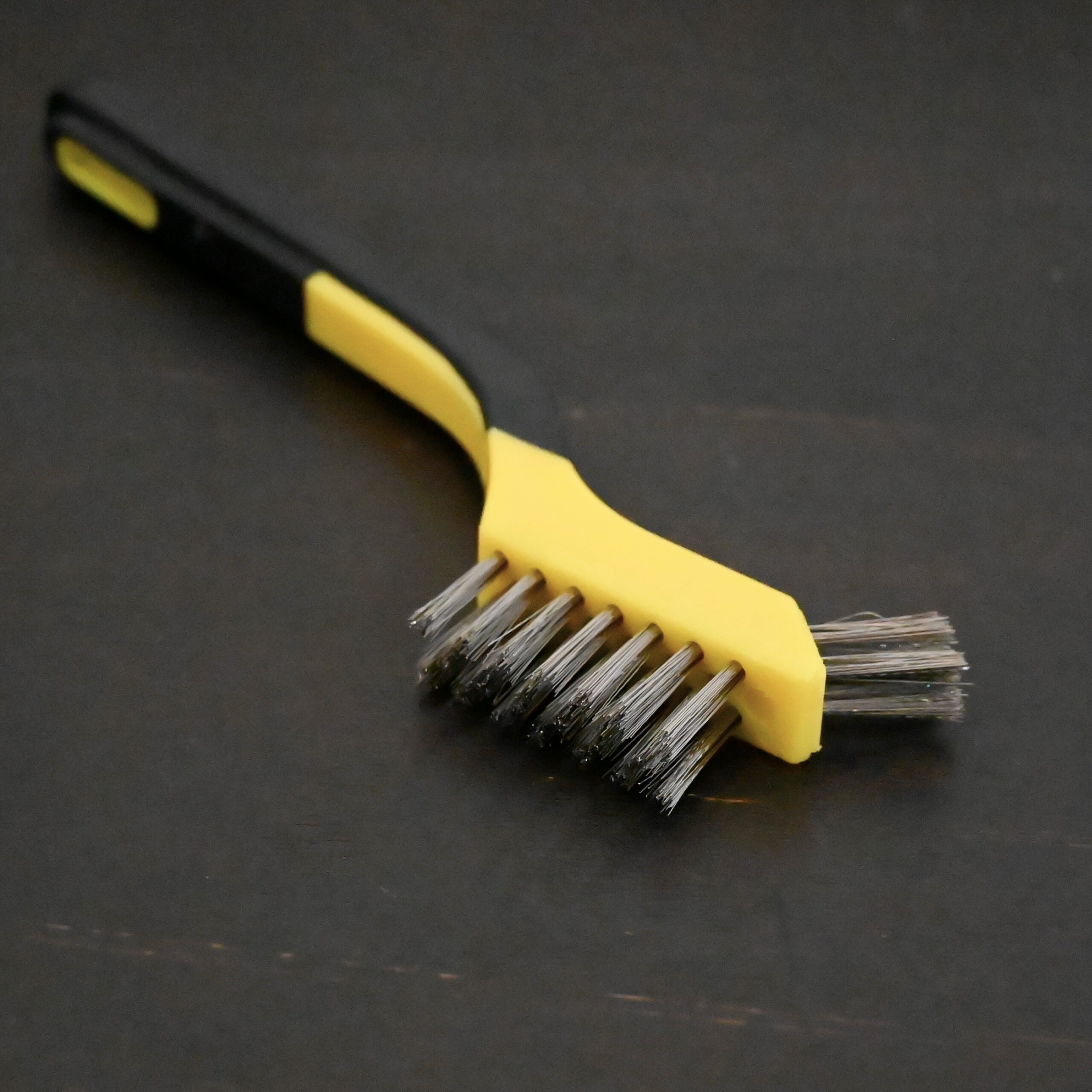 Stainless Steel Wire Brush - black and yellow plastic handle shown on dark background