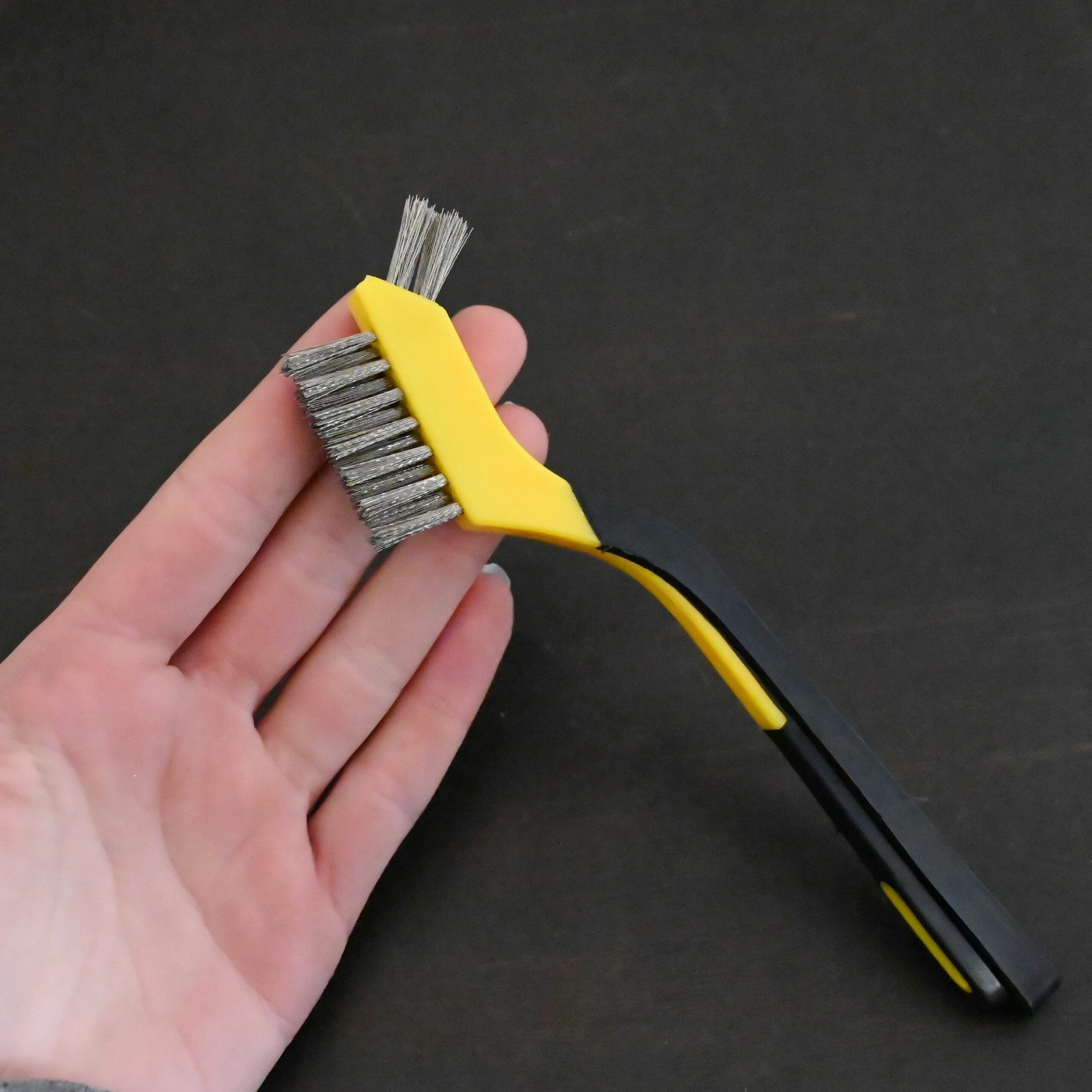 Stainless Steel Wire Brush - black and yellow plastic handle shown in hand