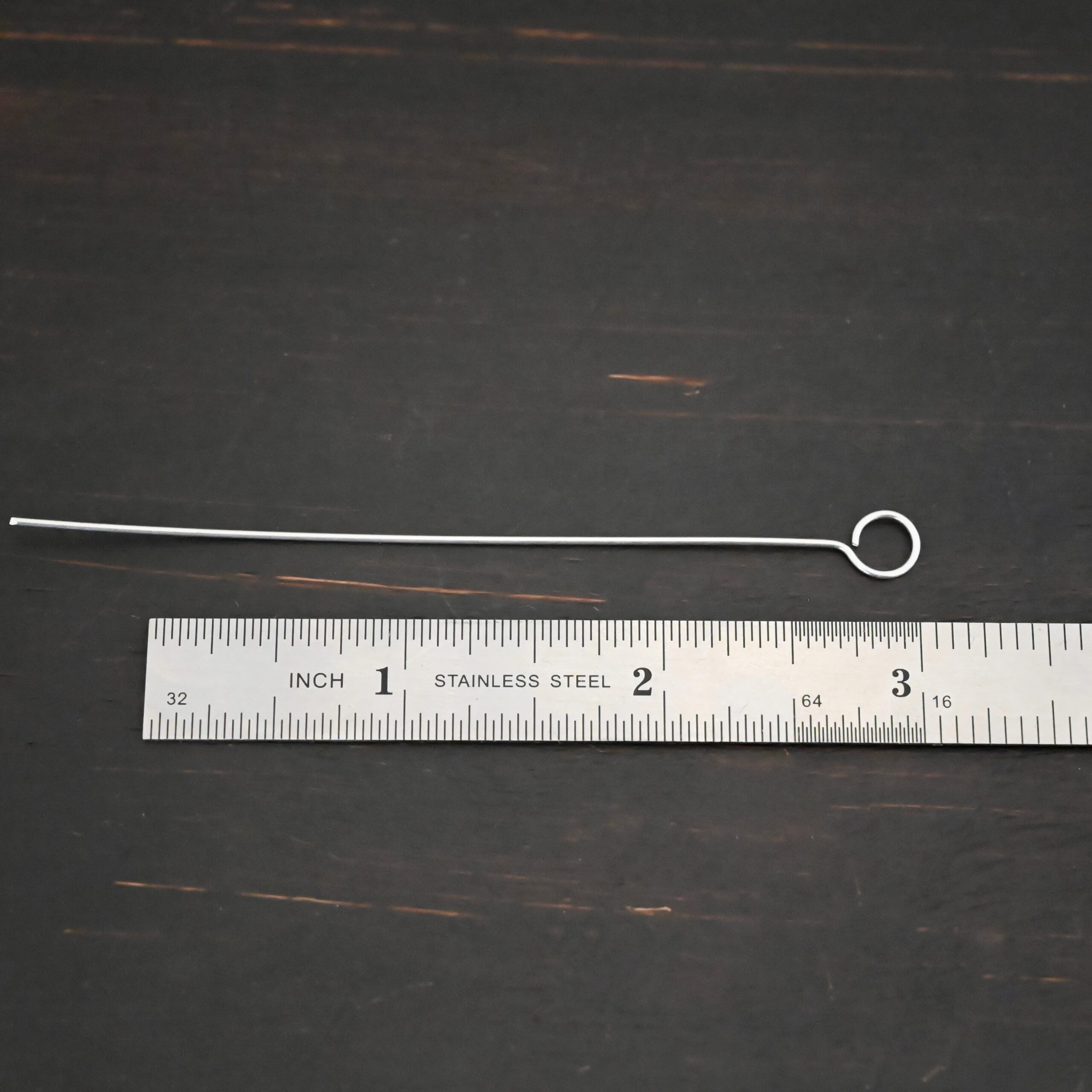 Silver shiny eye pin shown by ruler