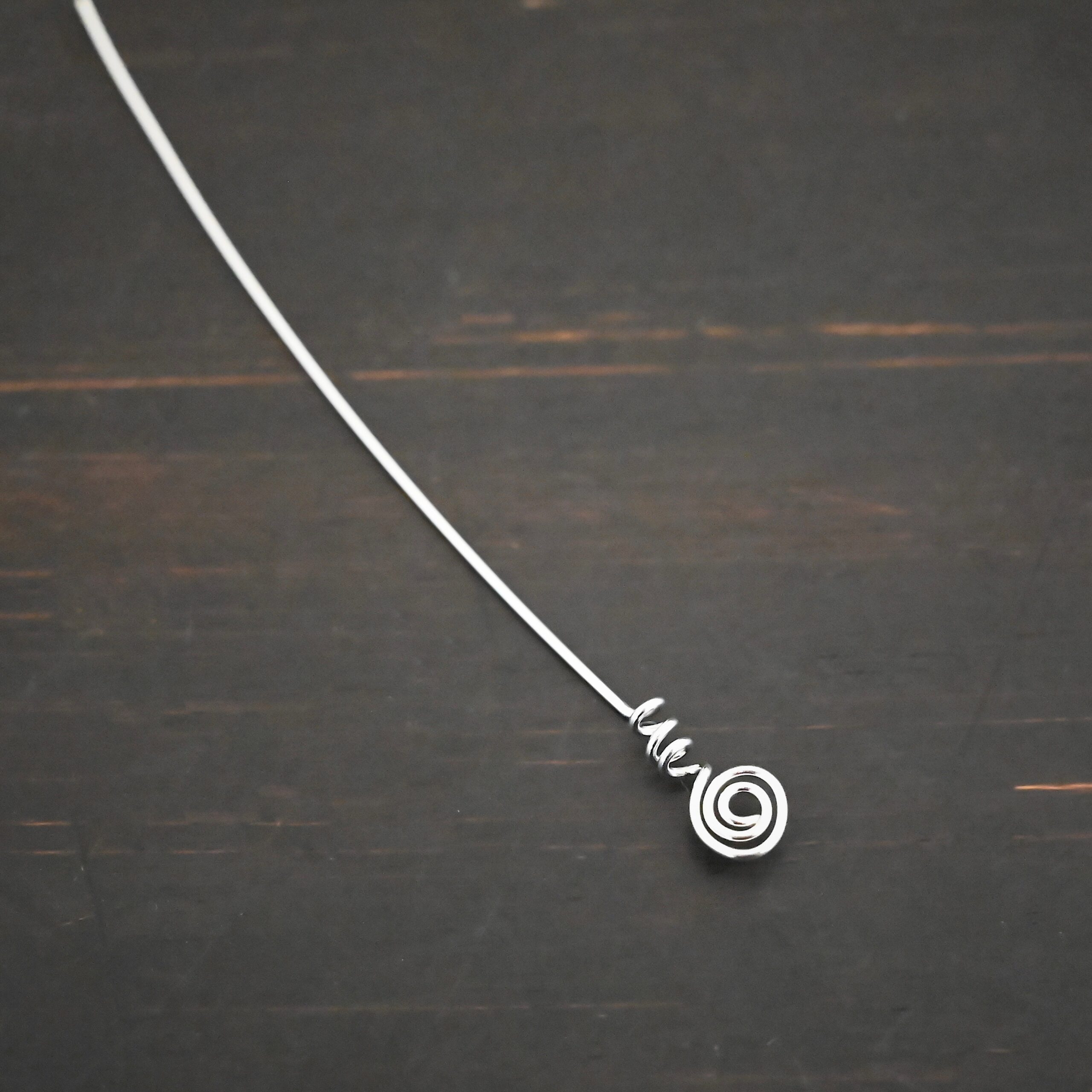 Silver shiny swirl headpin shown on dark background