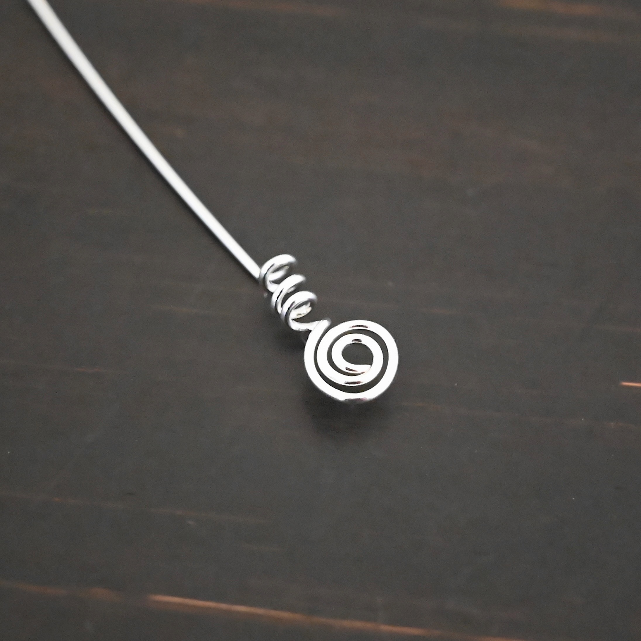 Silver shiny swirl headpin shown on dark background