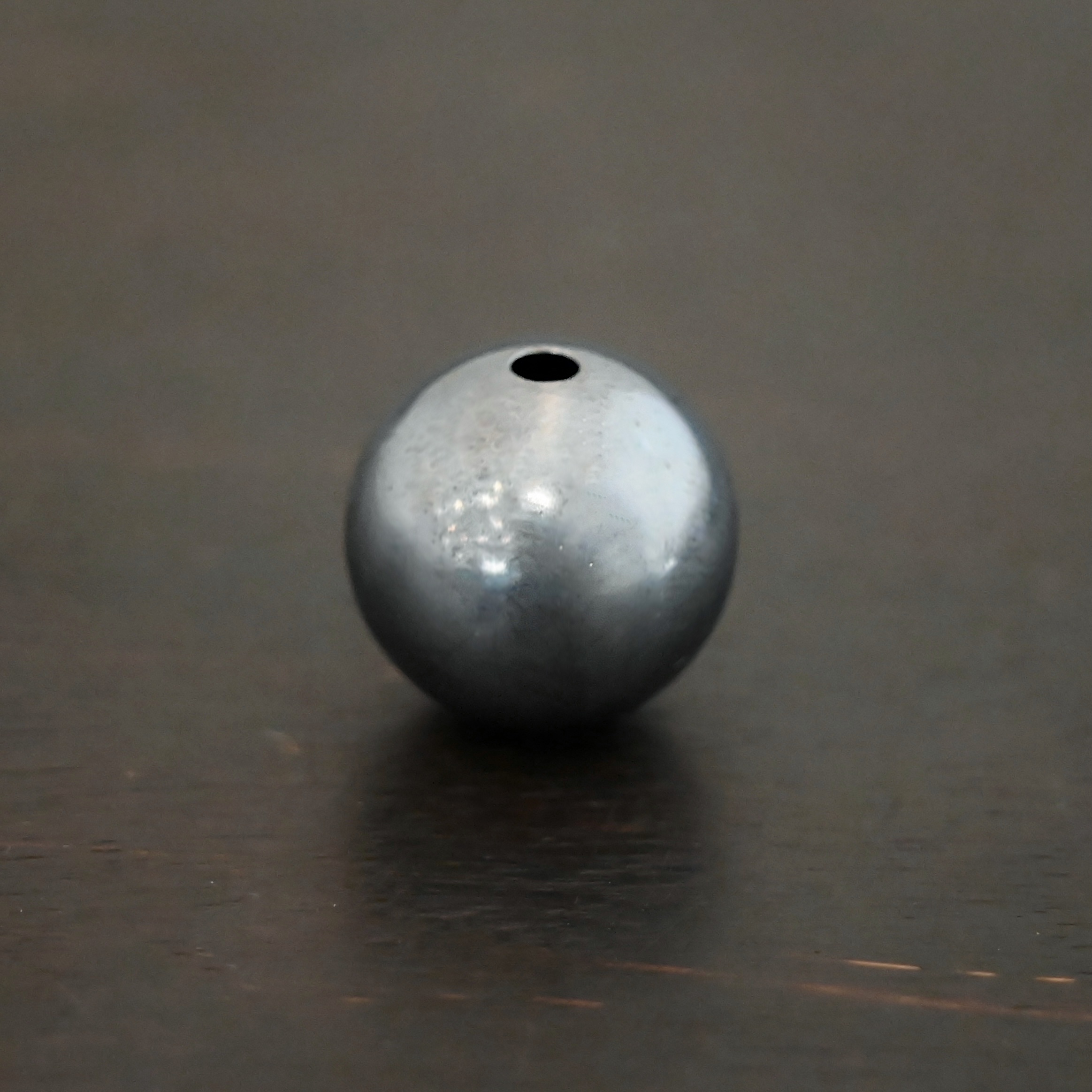 Silver oxidized hollow bead shown on dark background