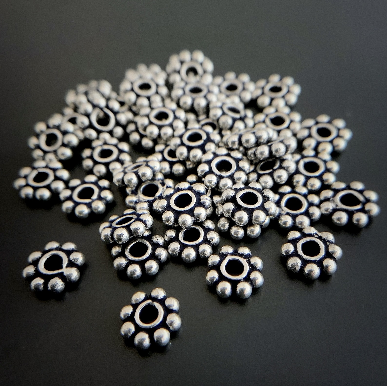 Silver daisy spacer shown on dark background