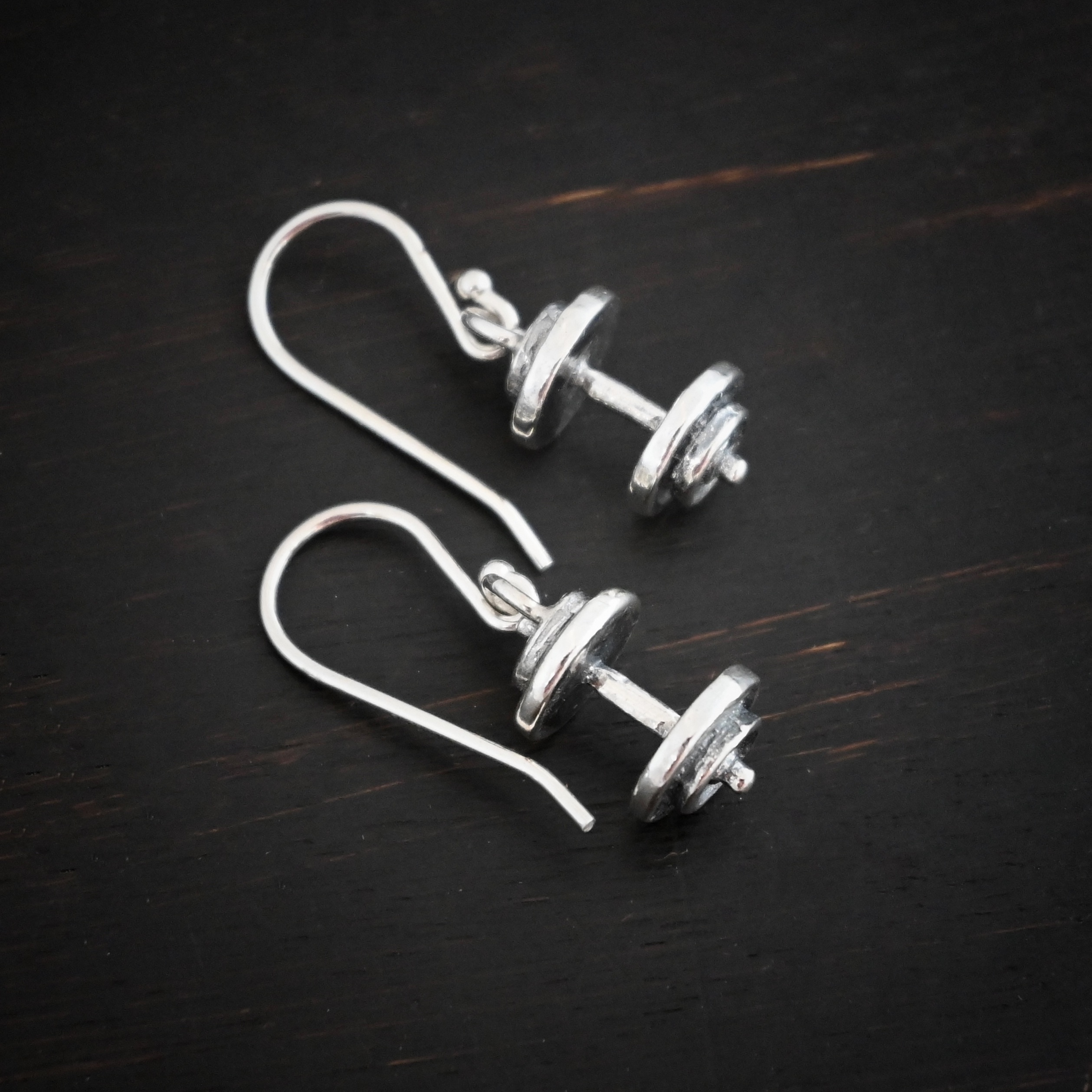 Silver barbell charm earrings shown on dark background
