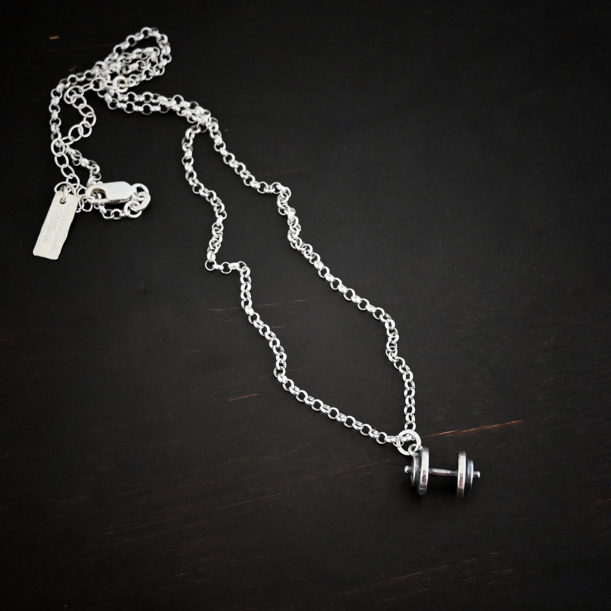 Silver barbell charm necklace shown on dark background