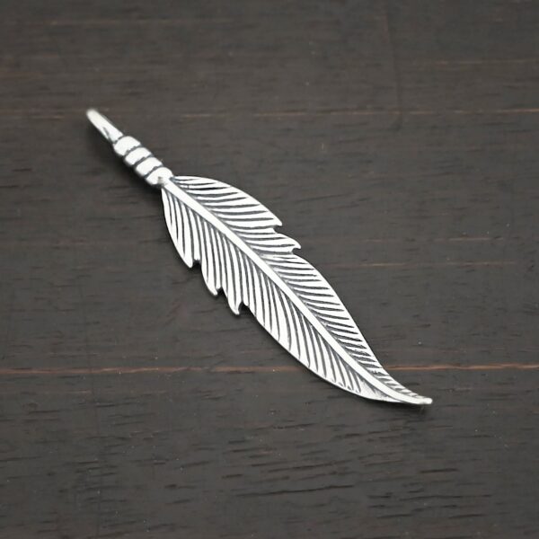 Silver shiny double sided feather charm shown on dark background