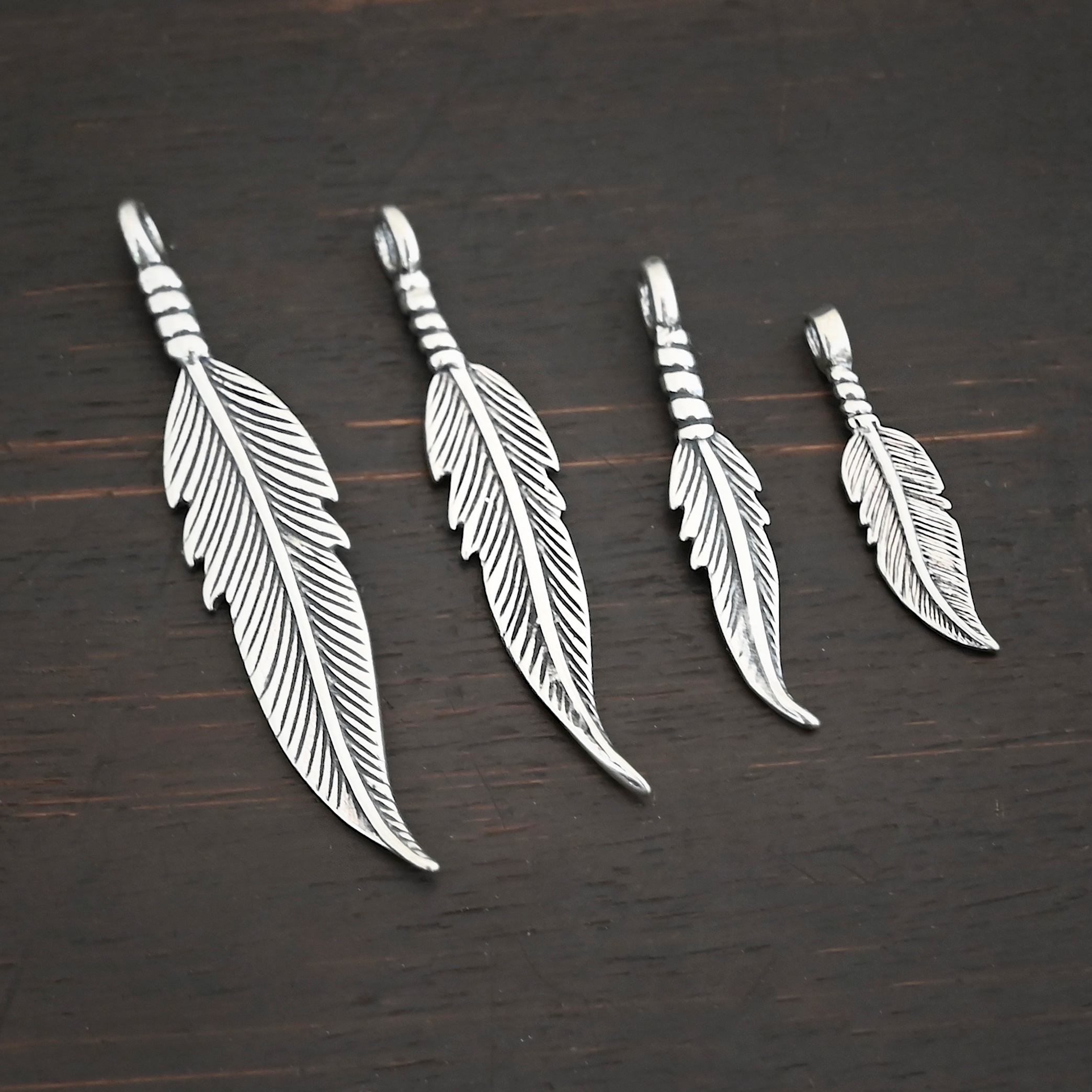 Silver shiny double sided feather charm shown on dark background