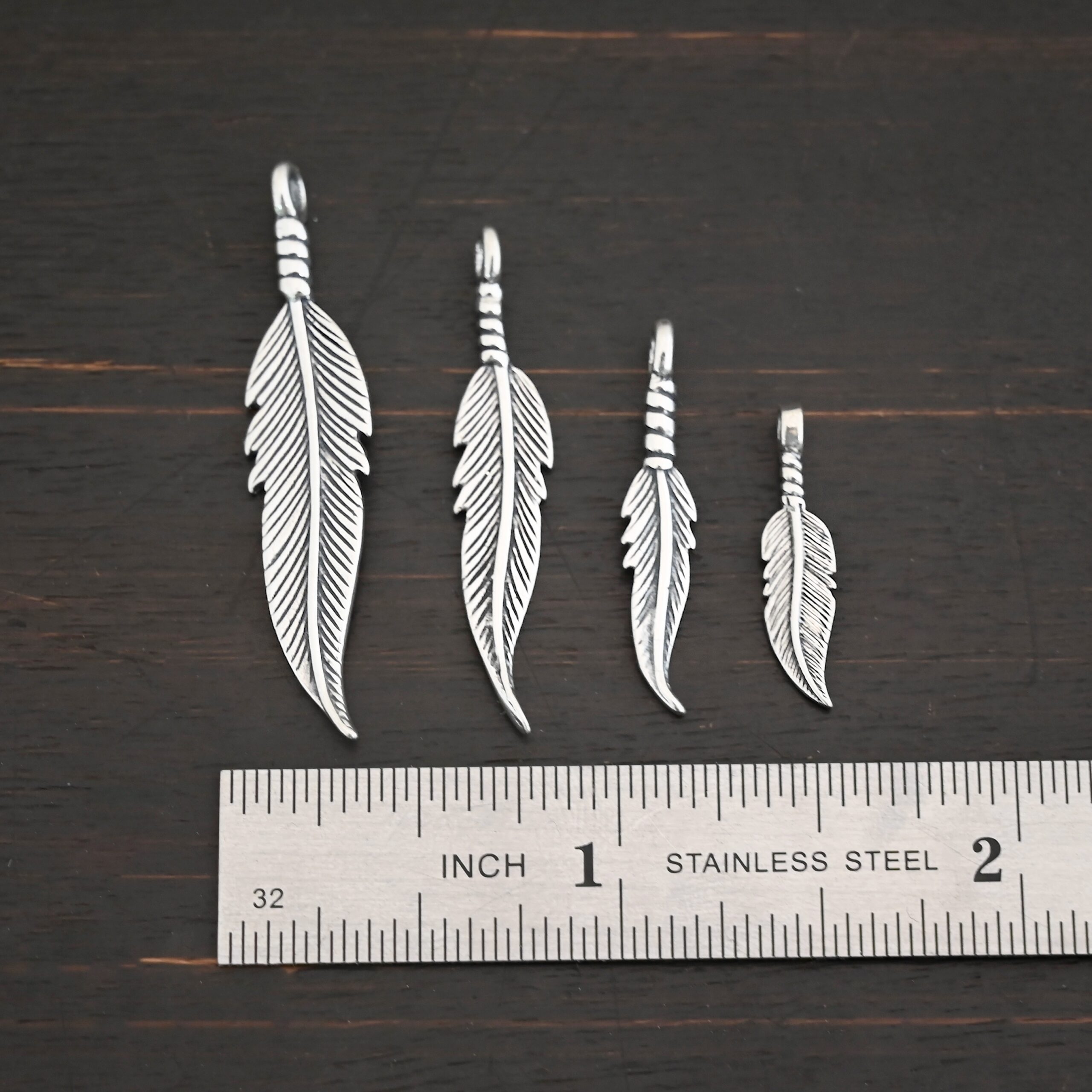 Silver shiny double sided feather charm shown next to ruler