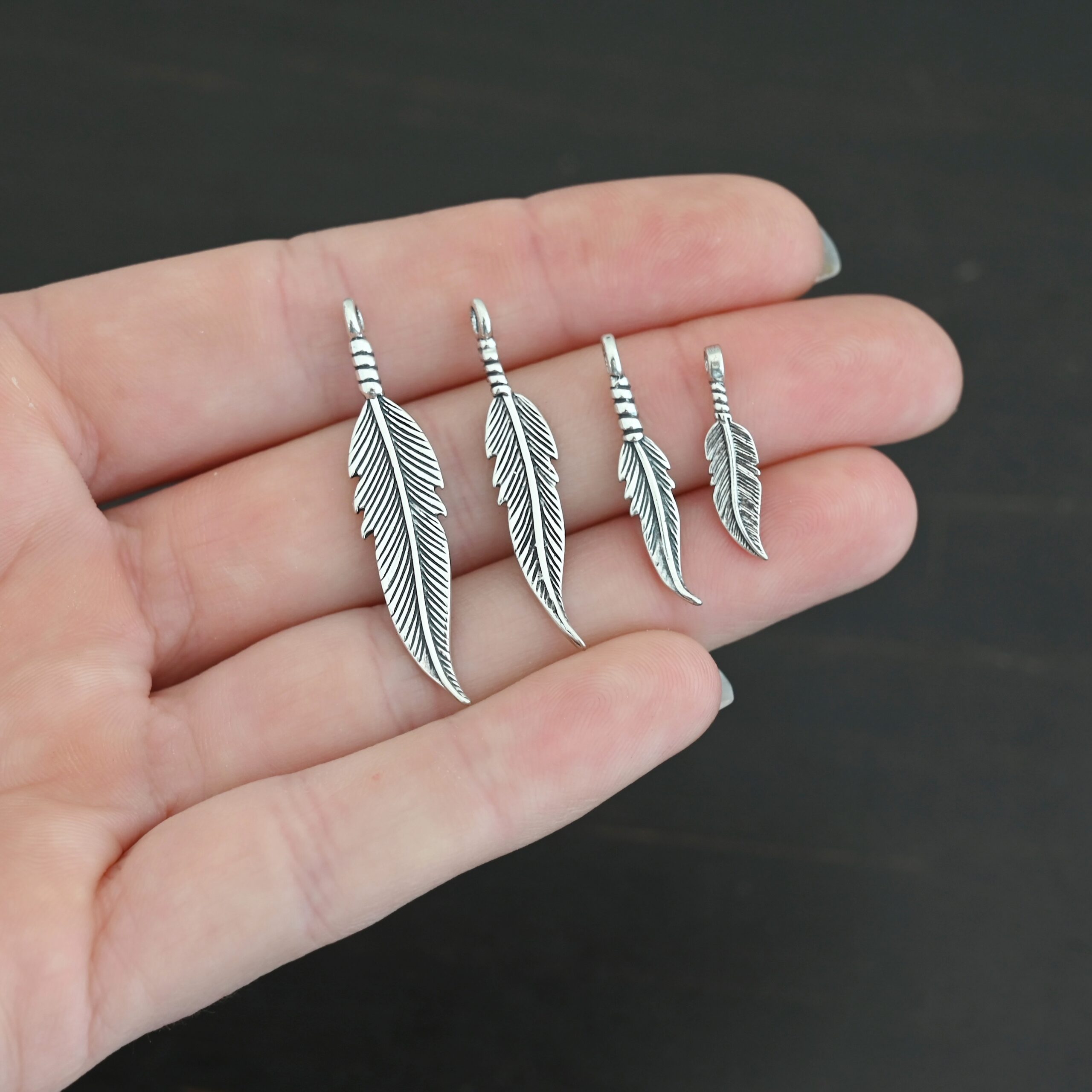 Silver shiny double sided feather charm shown in hand