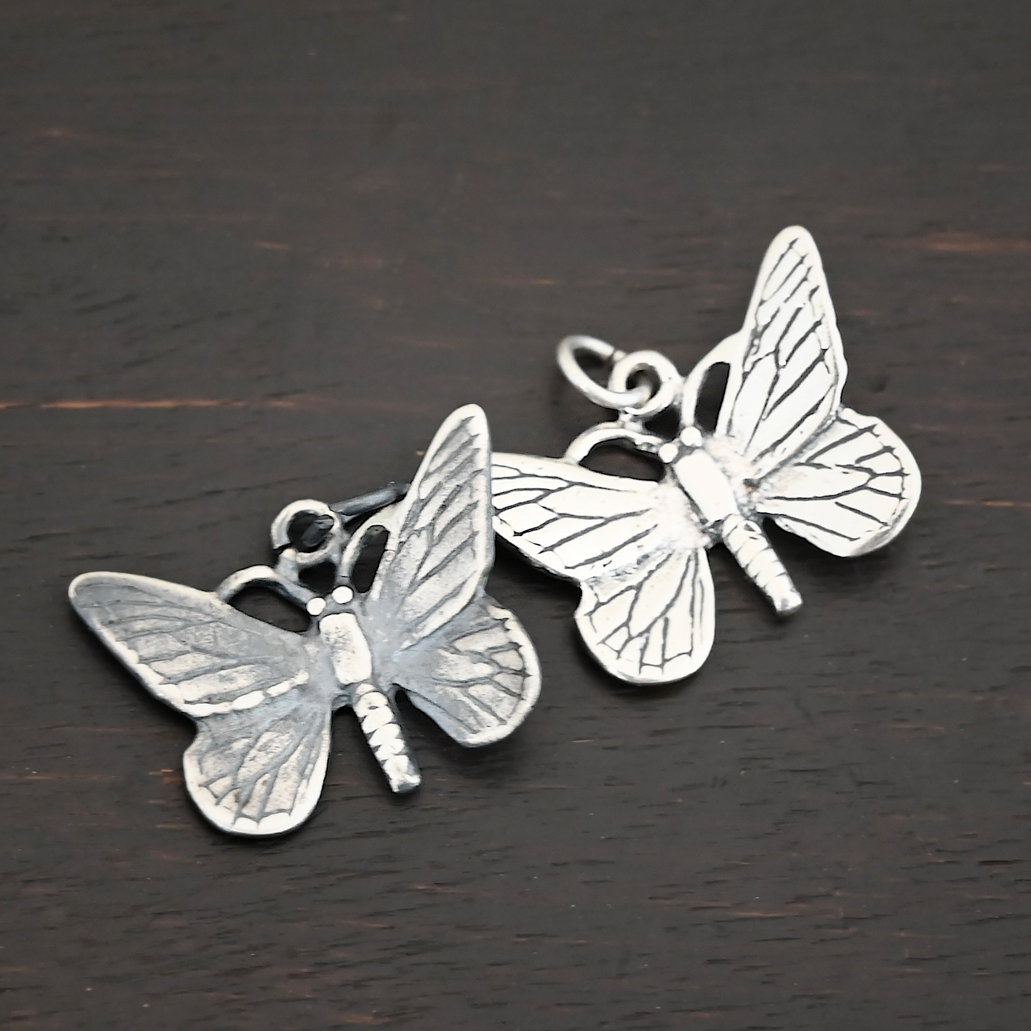 Silver oxidized and shiny butterfly charm shown on dark background