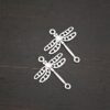 Silver shiny dragonfly charms shown on dark background