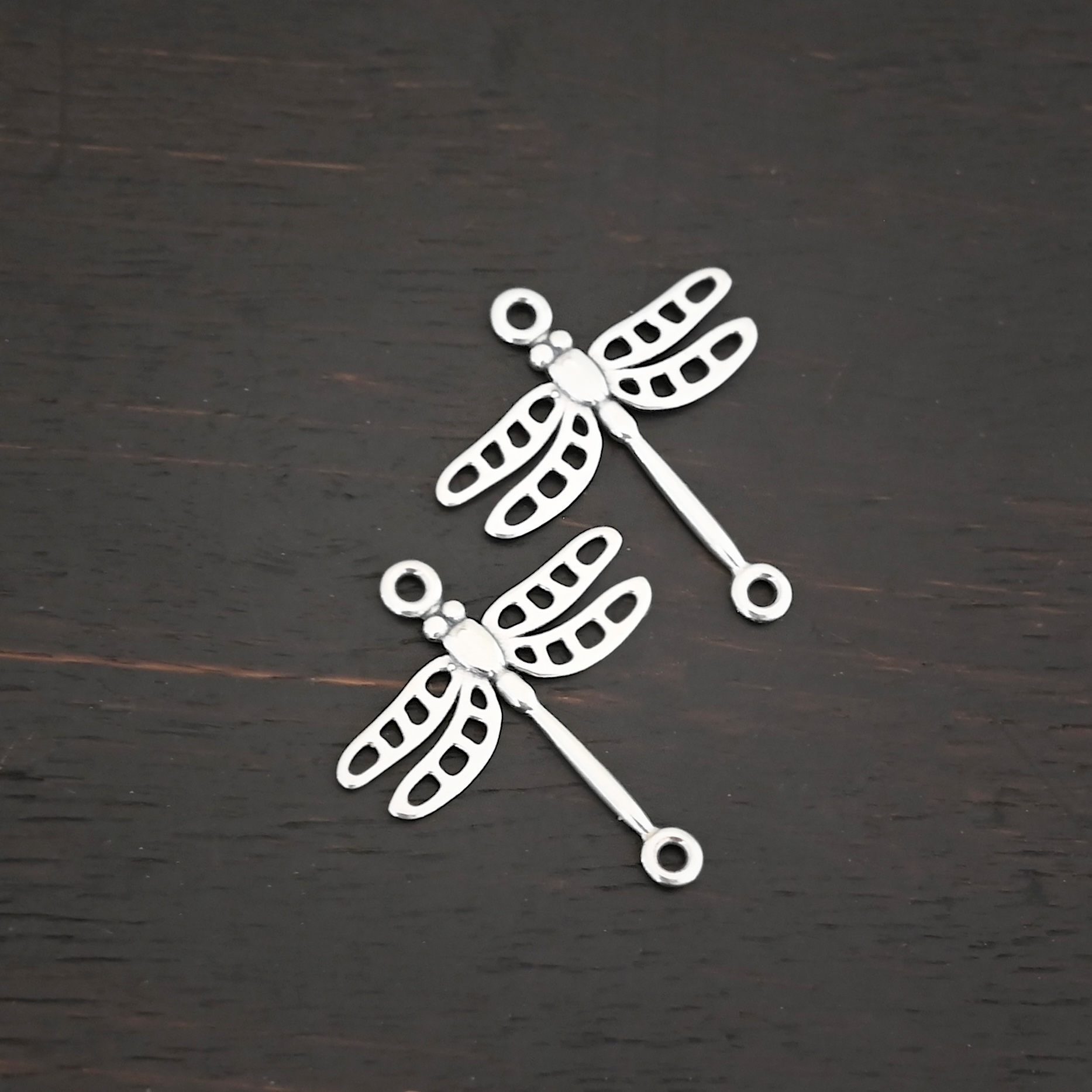 Silver shiny dragonfly charms shown on dark background