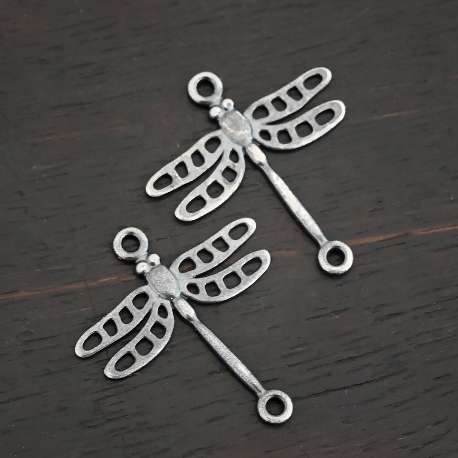 Silver oxidized dragonfly charms shown on dark background