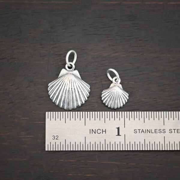 Silver sea shell charms shown by ruler