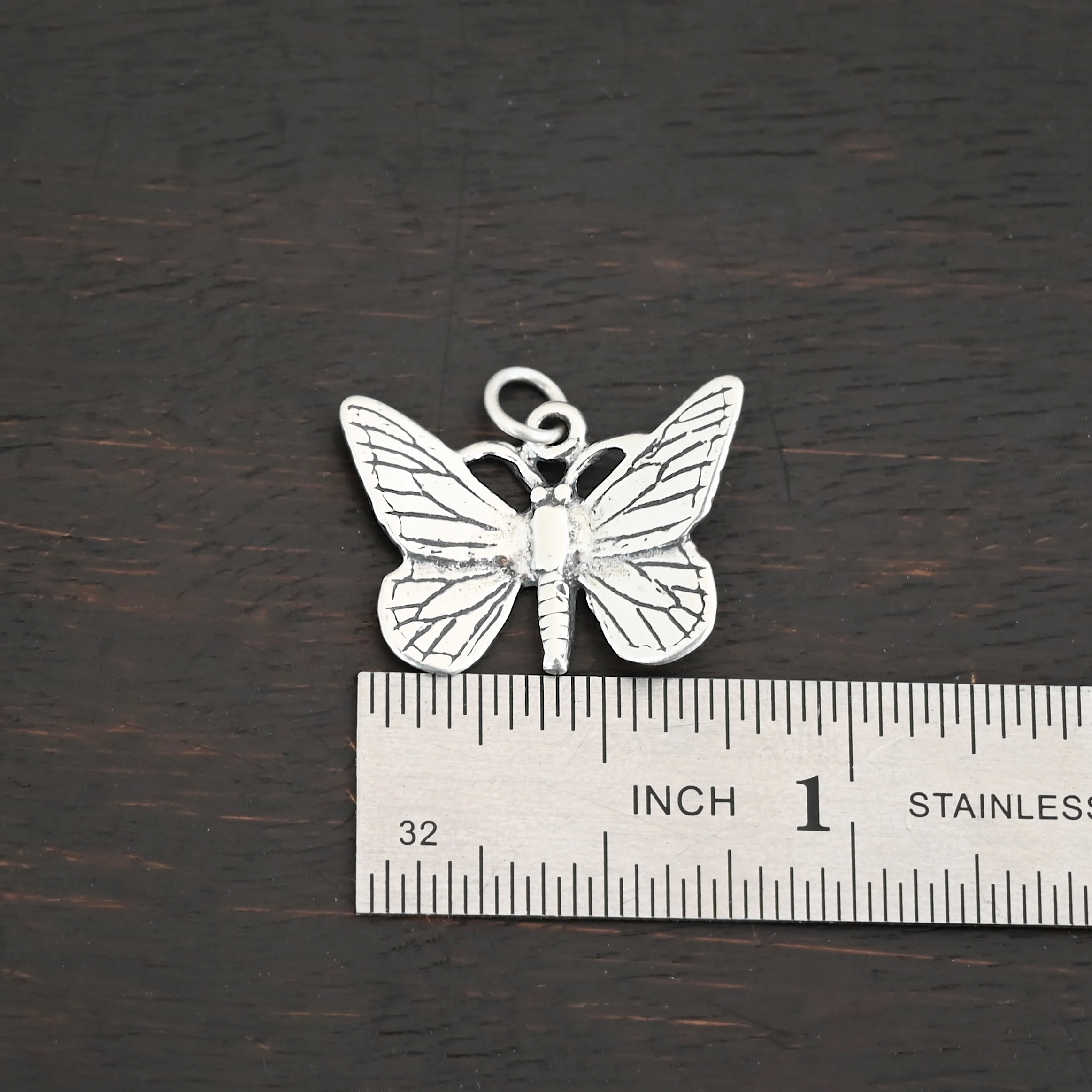 Silver shiny butterfly charm shown by ruler
