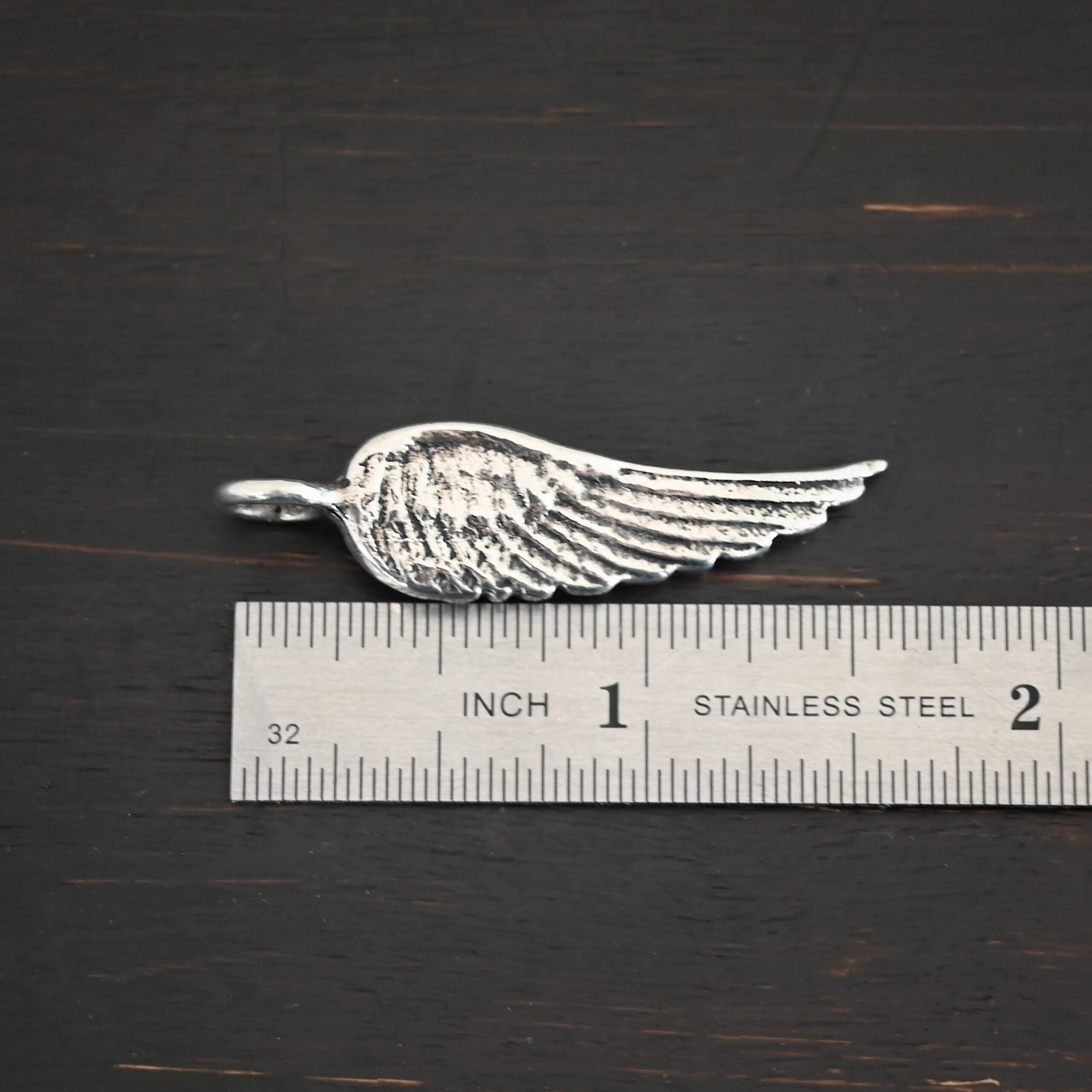 Silver Angel Wing charm shiny charm shown by ruler
