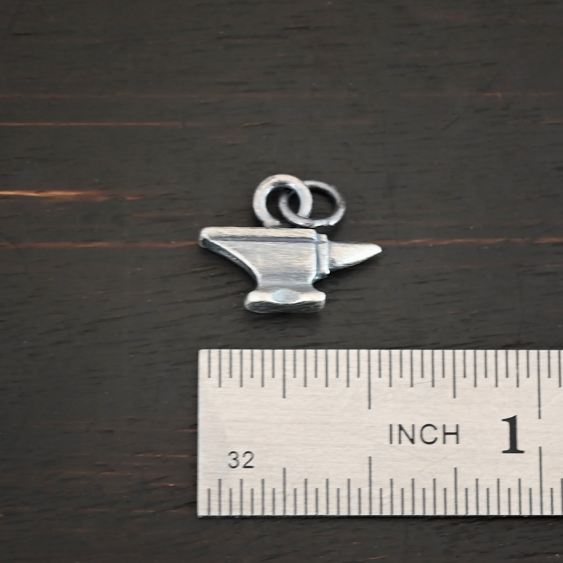 Silver anvil charm oxidized shown by ruler