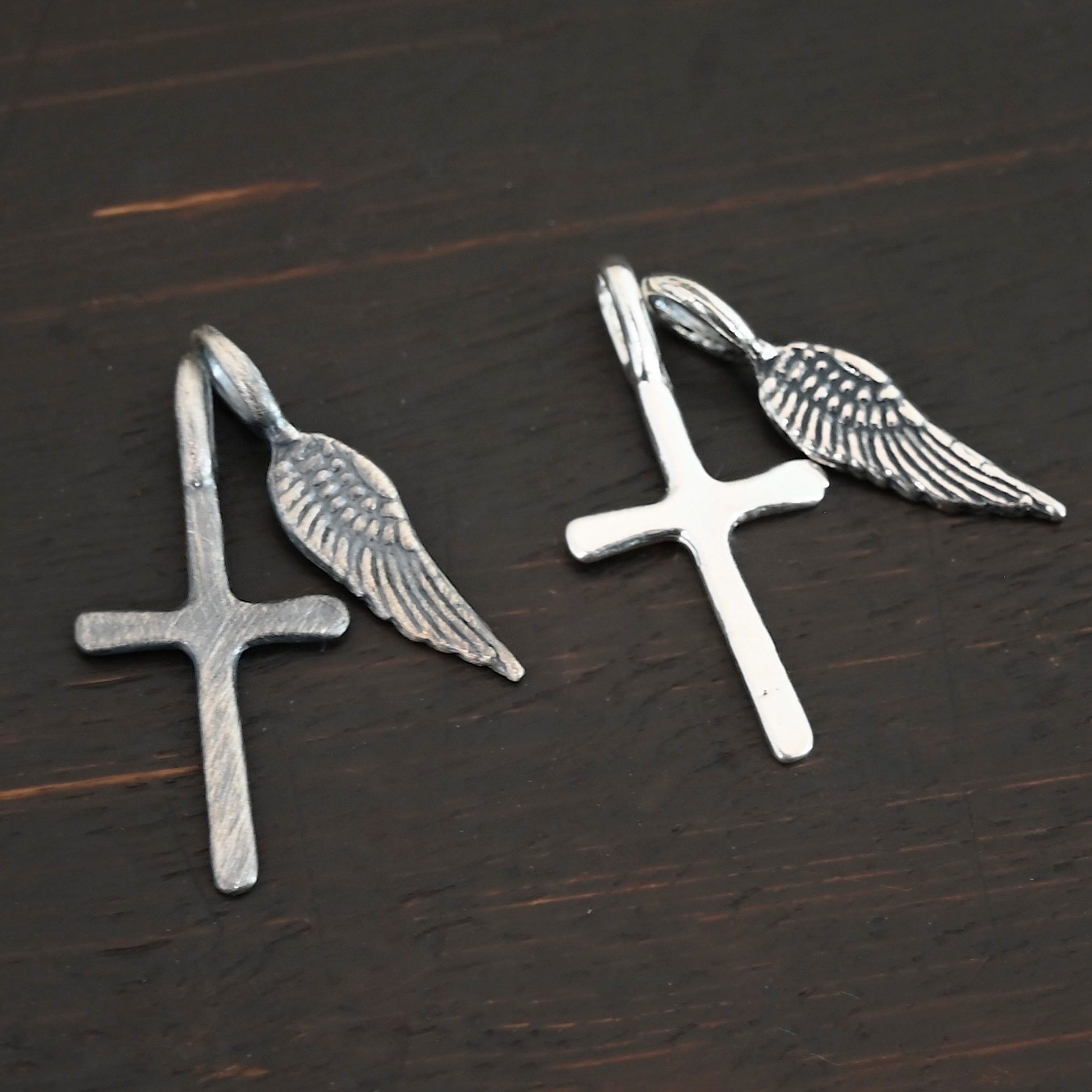 Silver small cross & angel wing charm oxidized & shiny shown on dark background