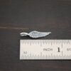 Silver small angel wing charm shiny shown by ruler