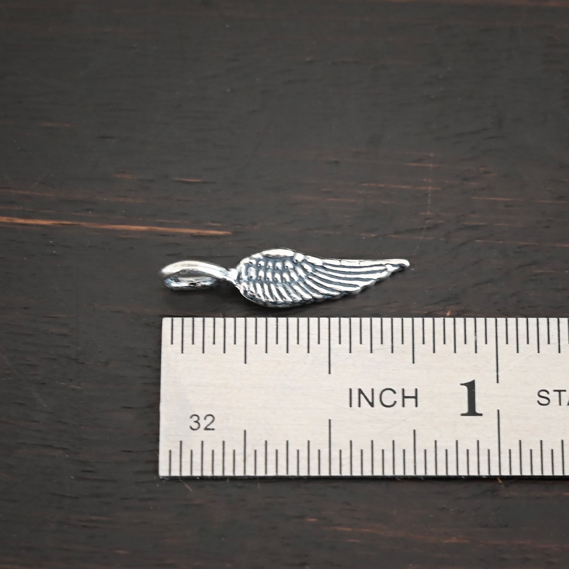 Silver small angel wing charm shiny shown by ruler