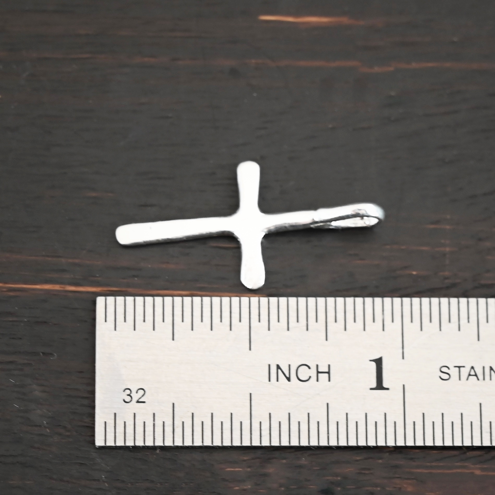 Silver small cross charm shiny shown by ruler