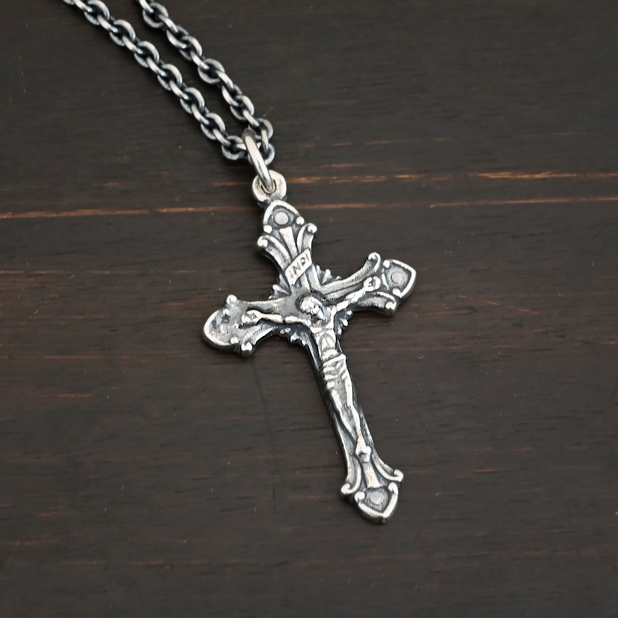 Silver crucifix pendant charm shown on chain on dark background