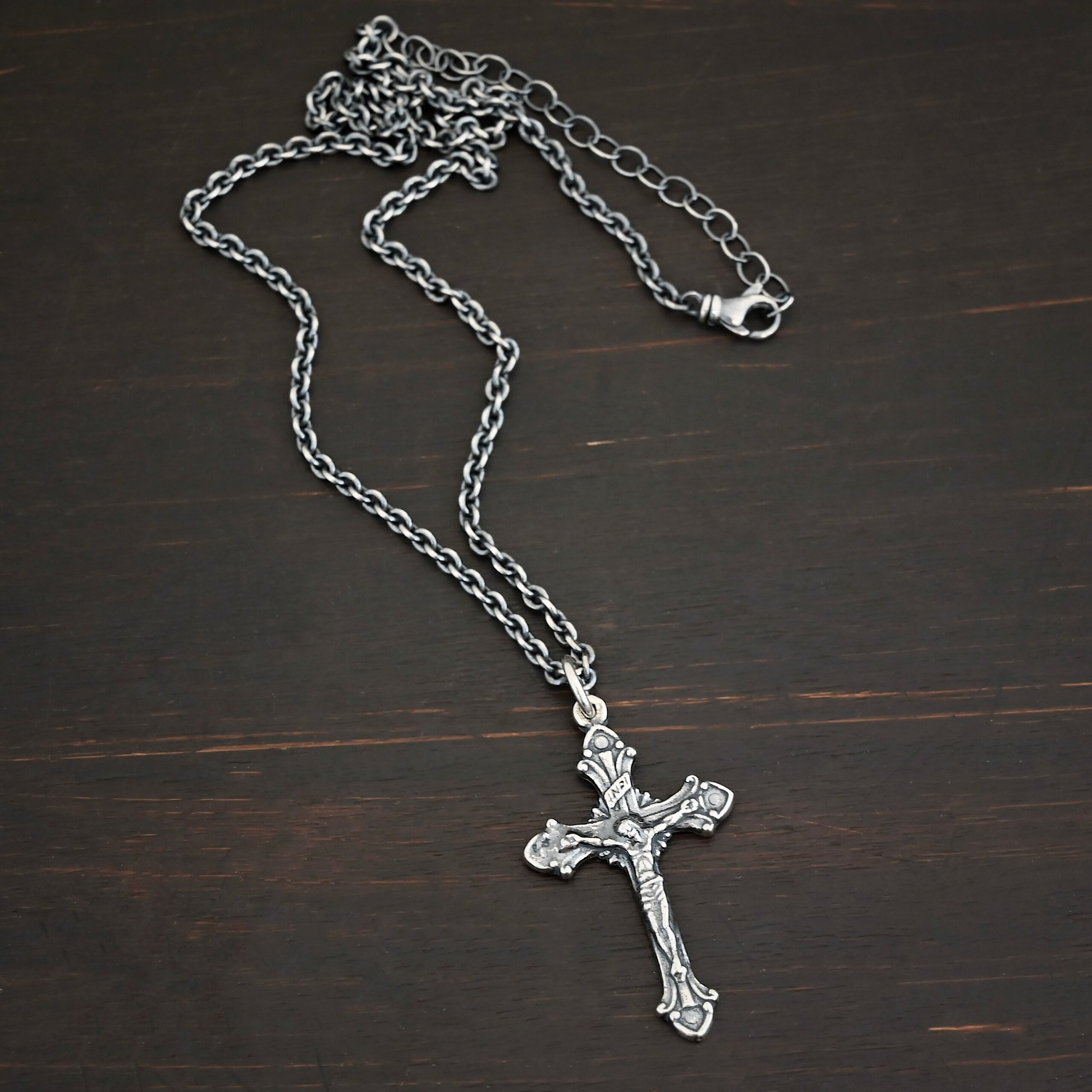 Silver crucifix pendant charm shown on chain on dark background