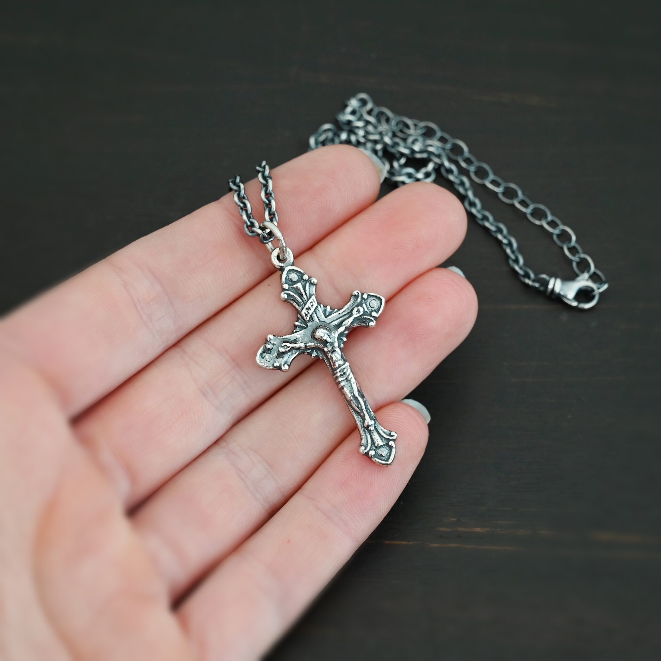 Silver crucifix pendant charm shown on chain in hand