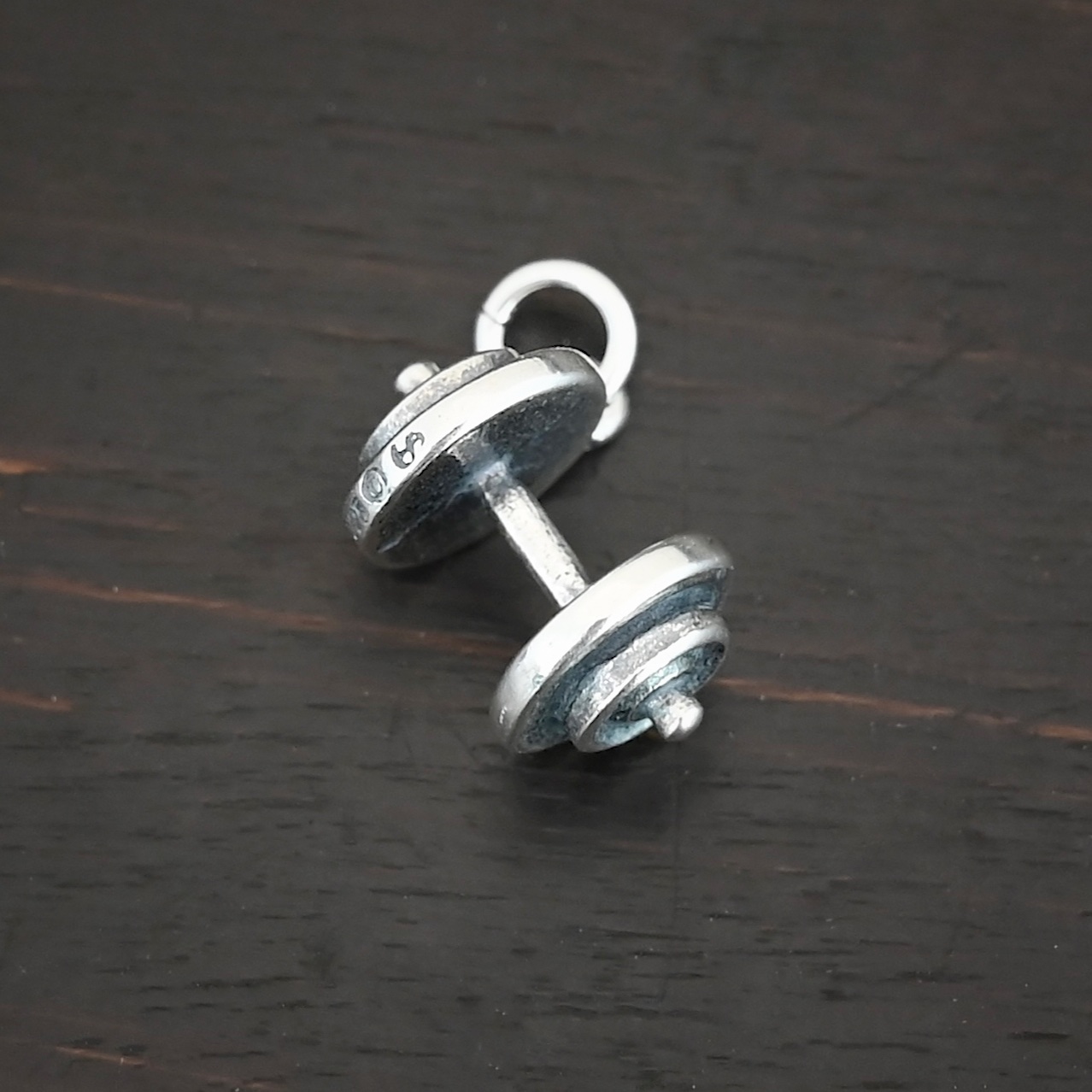 Silver dumbbell charm shown on dark background