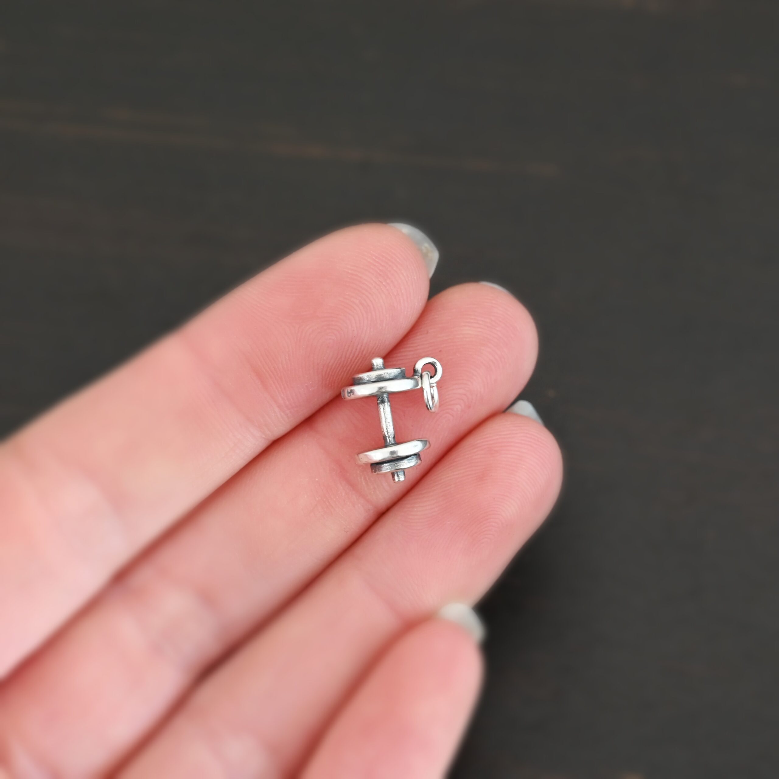 Silver dumbbell charm shown in hand