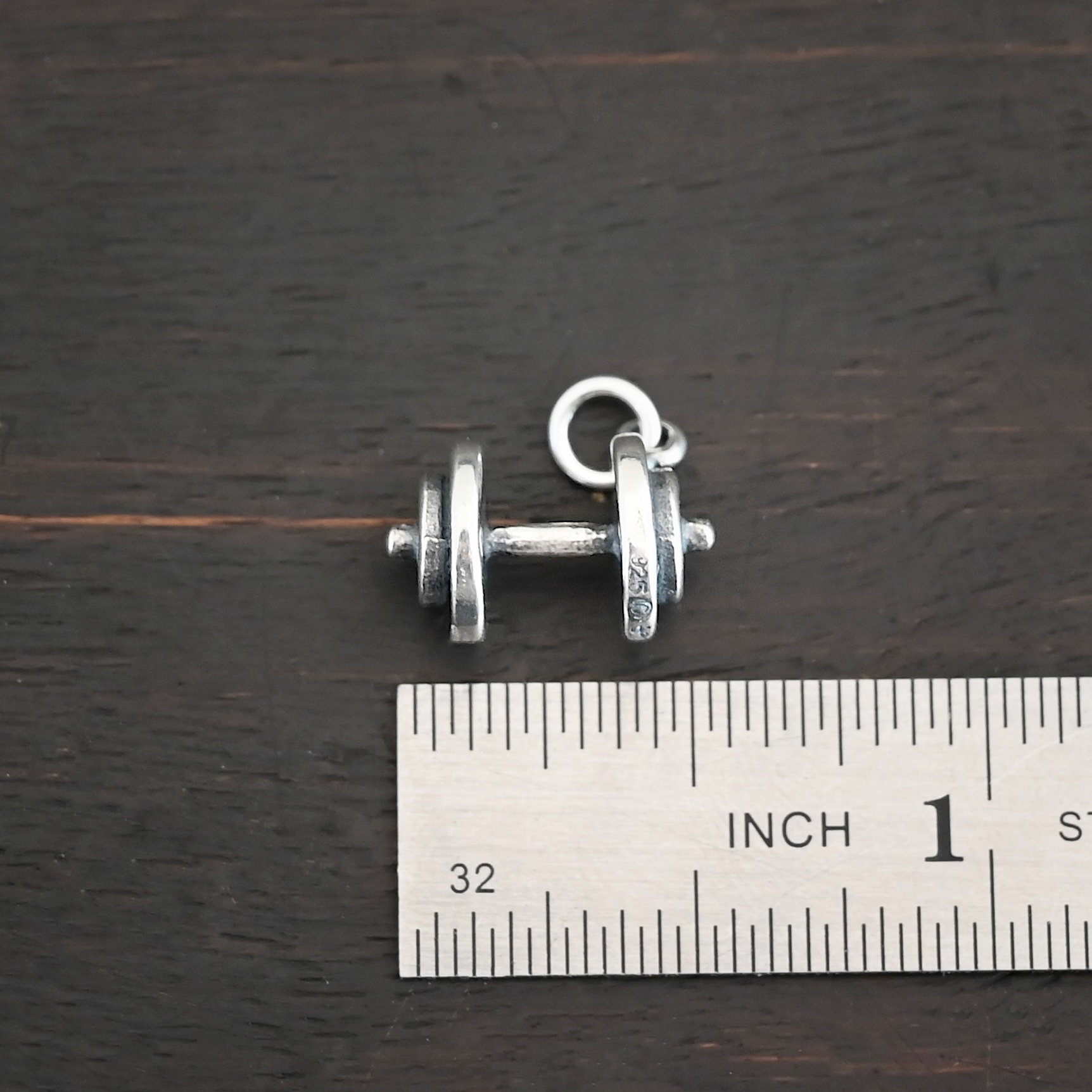 Silver dumbbell charm shown by ruler