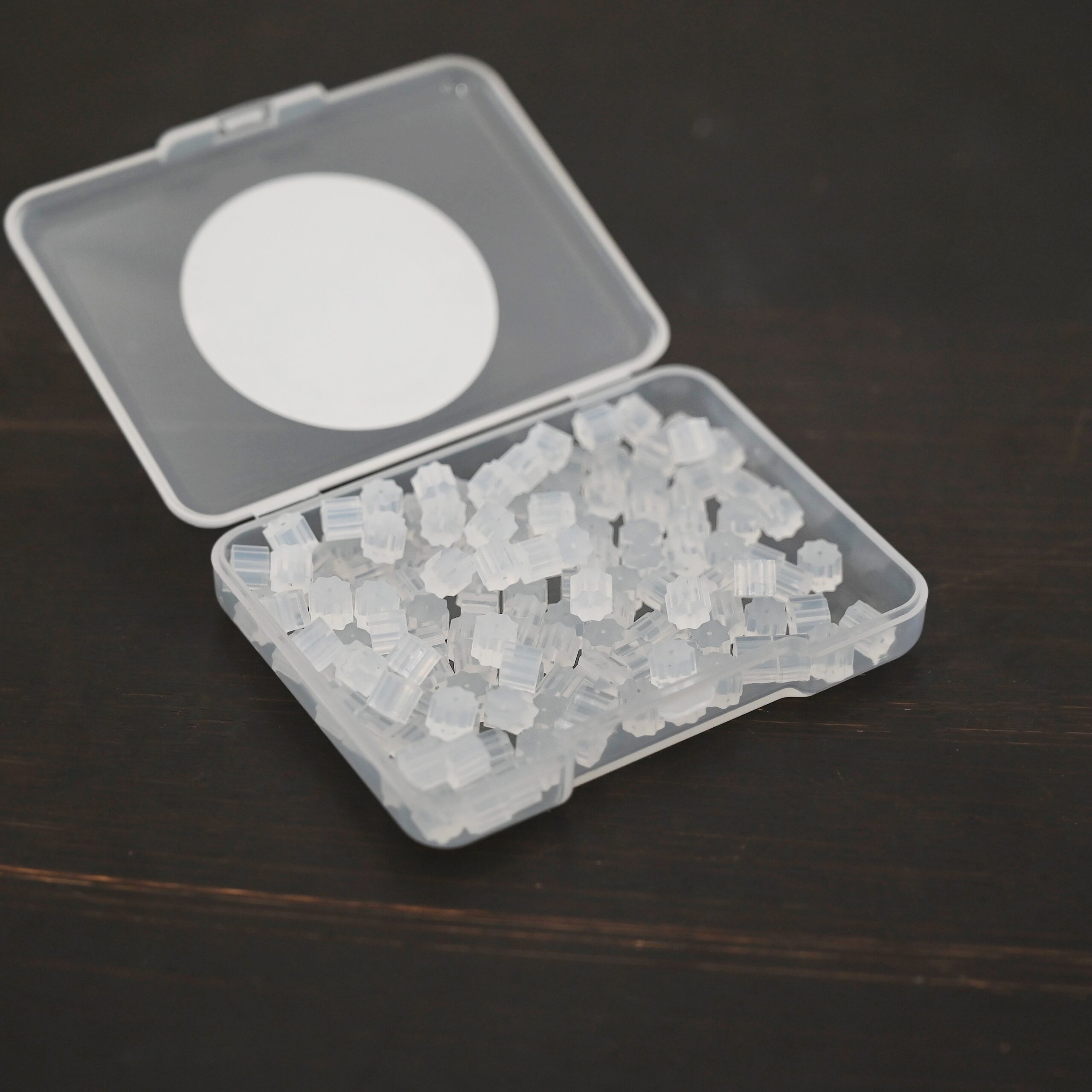 Rubber Earring Backs shown in plastic container on dark background