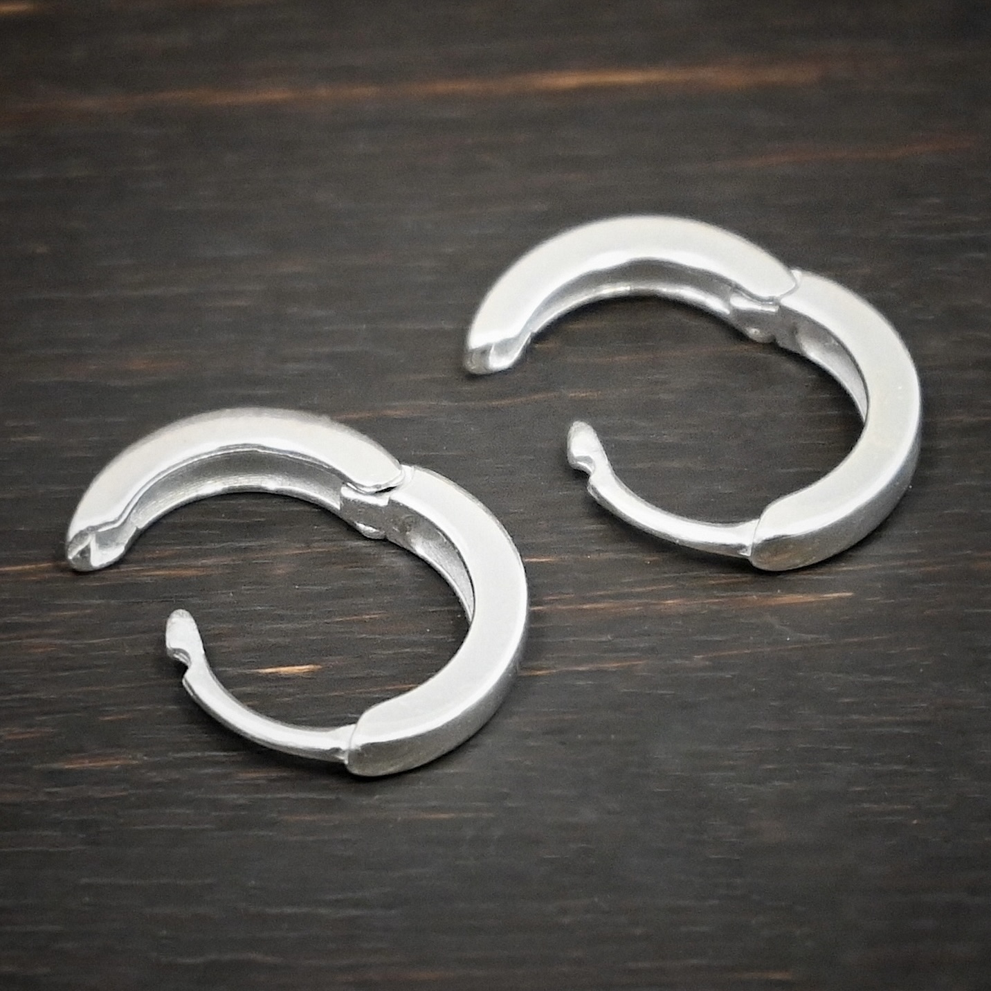 Winona Huggie Hoops Earrings - shiny sterling silver Winona Huggie Hoop Earrings - shiny shown on dark background