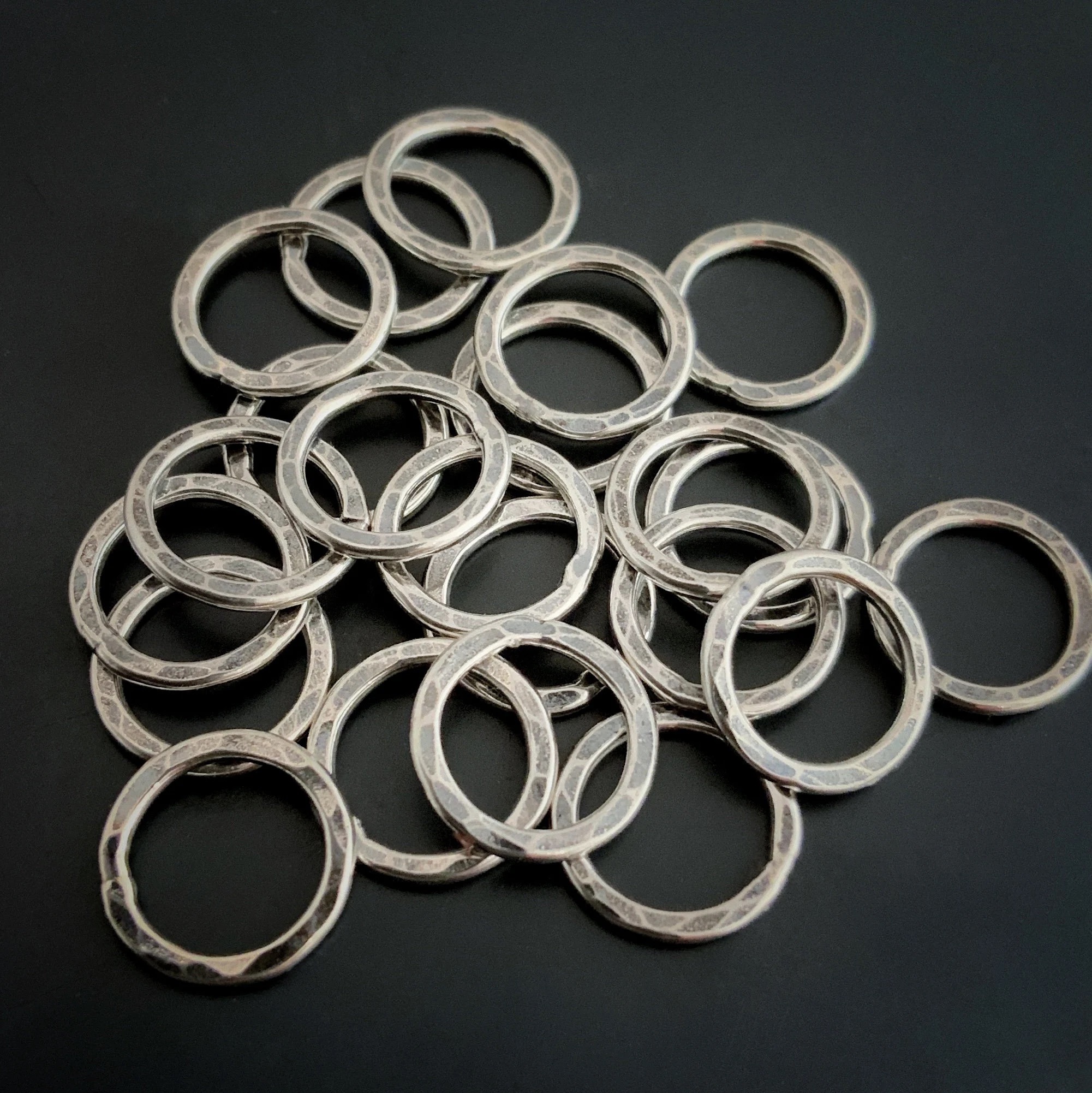 Pile of jump rings against a dark background. They are hammered and oxidized
