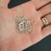 Pile of jump rings. They are shiny, smooth, and open. They are shown in the palm of a hand.