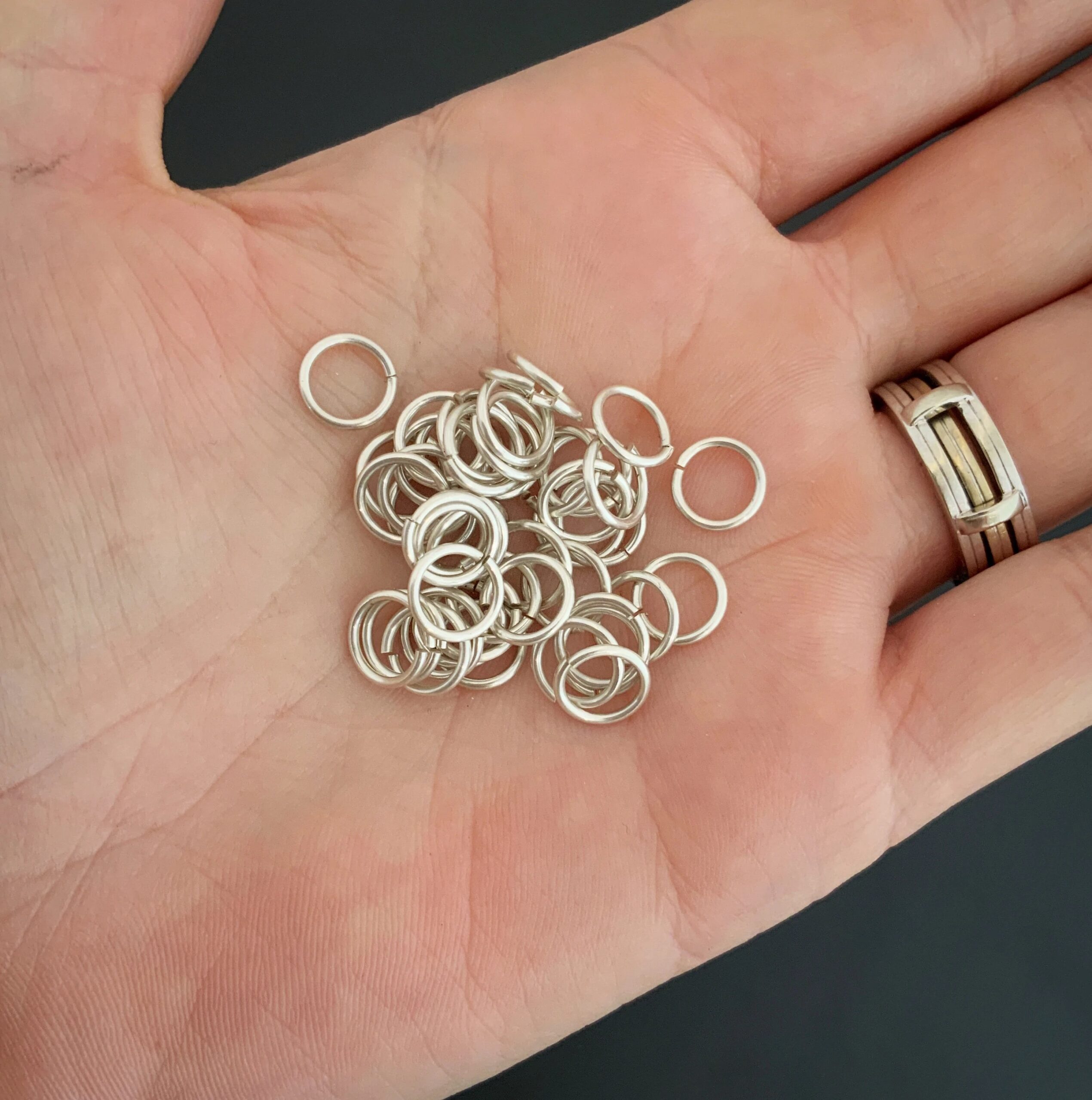 Pile of jump rings. They are shiny, smooth, and open. They are shown in the palm of a hand.