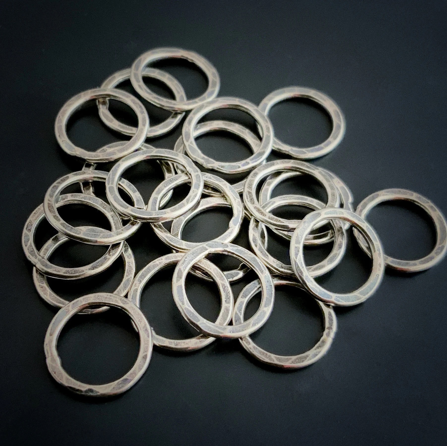 Pile of jump rings against a dark background. They are hammered and oxidized