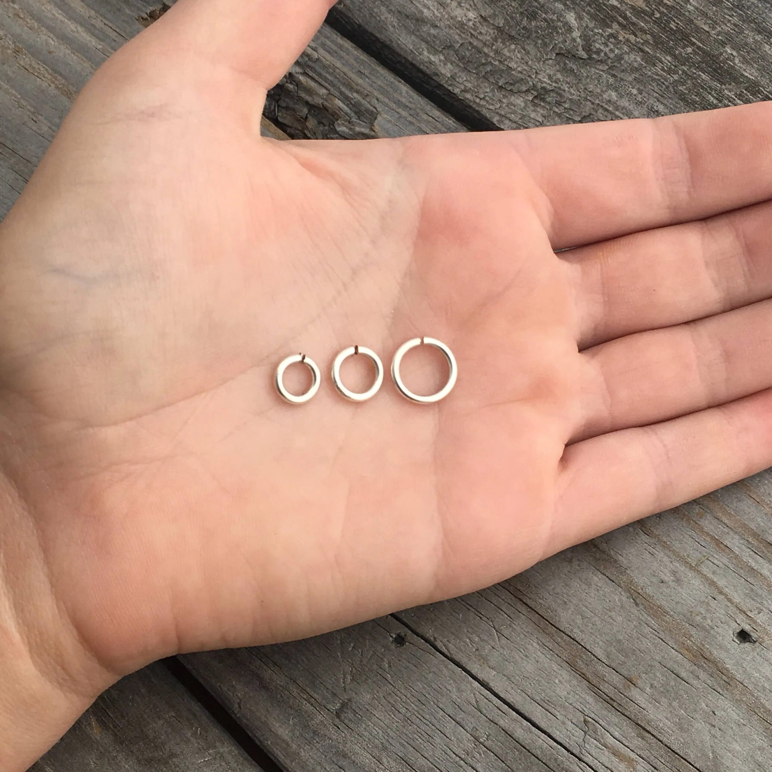 Three jump rings shown in the palm of a hand. They are shiny, smooth, and open. They go from smallest to biggest.