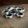 Pile of thick oxidized jump rings against a rusted metal background.