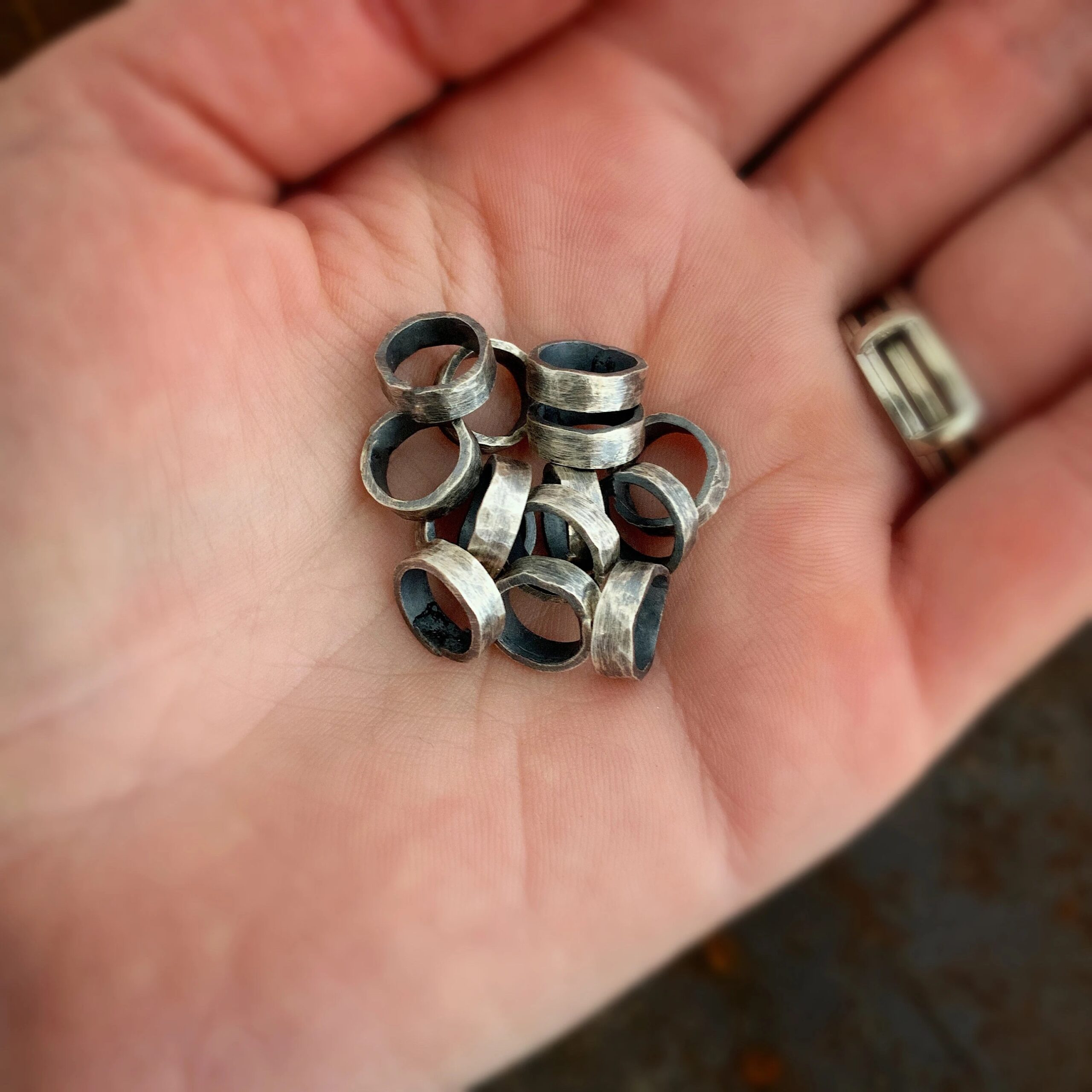 Image 28 Pile of thick oxidized jump rings lying in the palm of a hand.