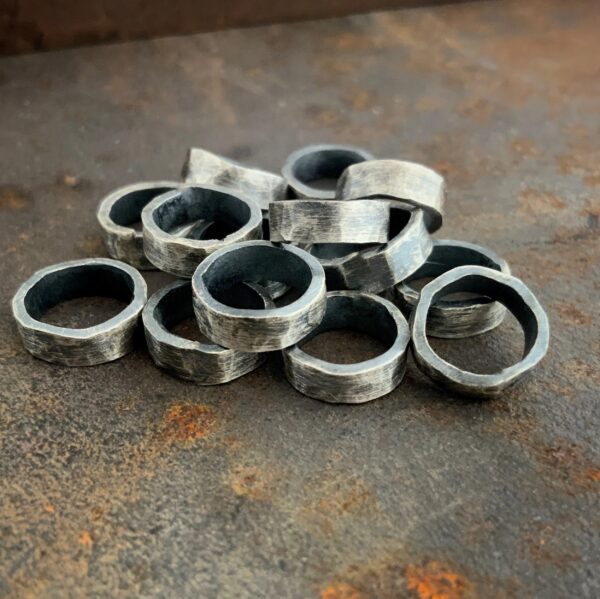 Pile of thick oxidized jump rings against a rusted metal background.