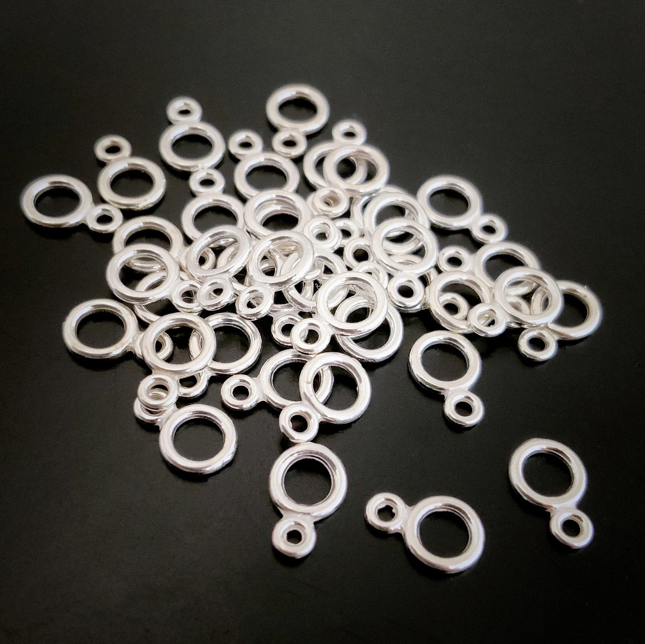 Pile of sterling silver double jump rings that are shiny against a dark background.