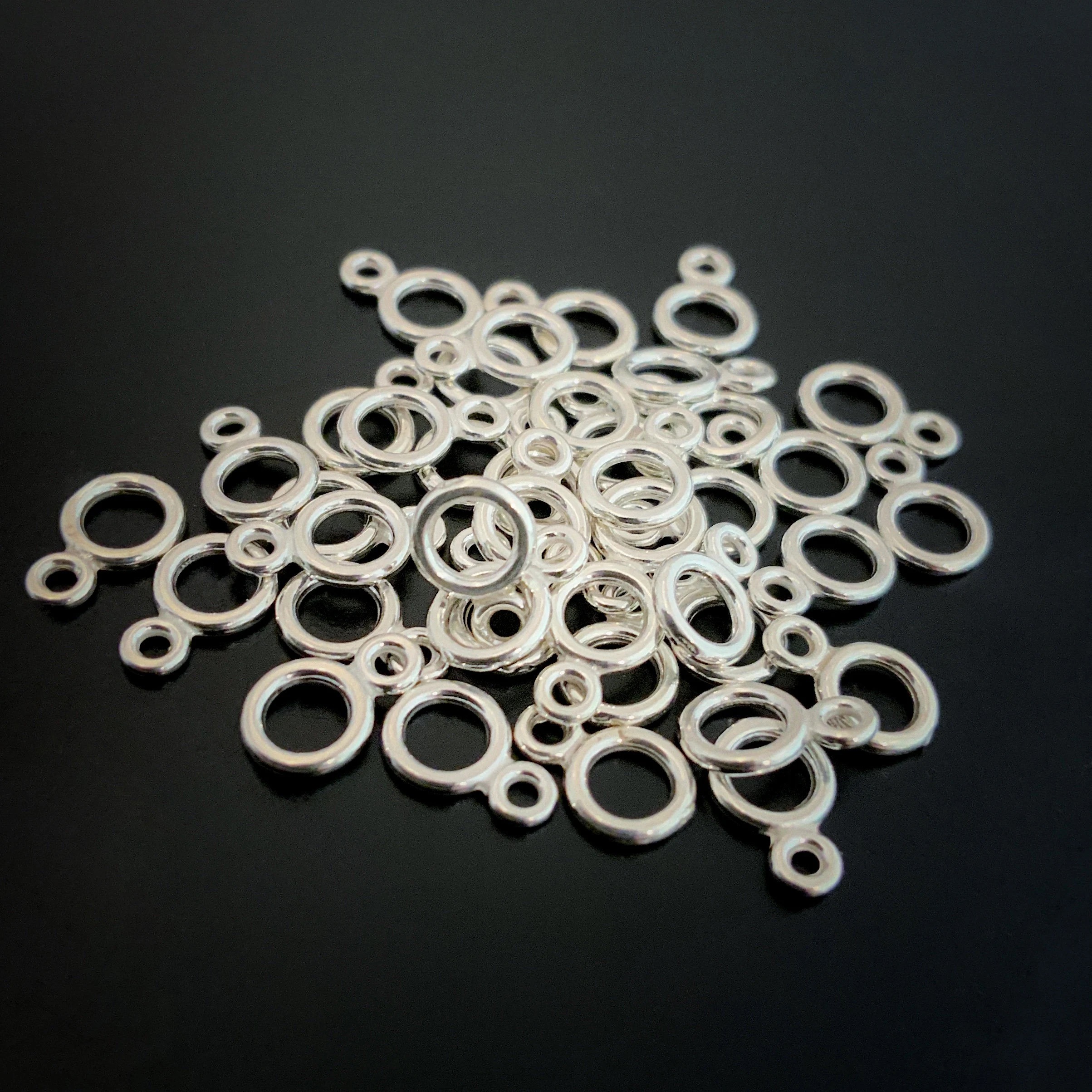 Pile of sterling silver double jump rings that are shiny against a dark background.