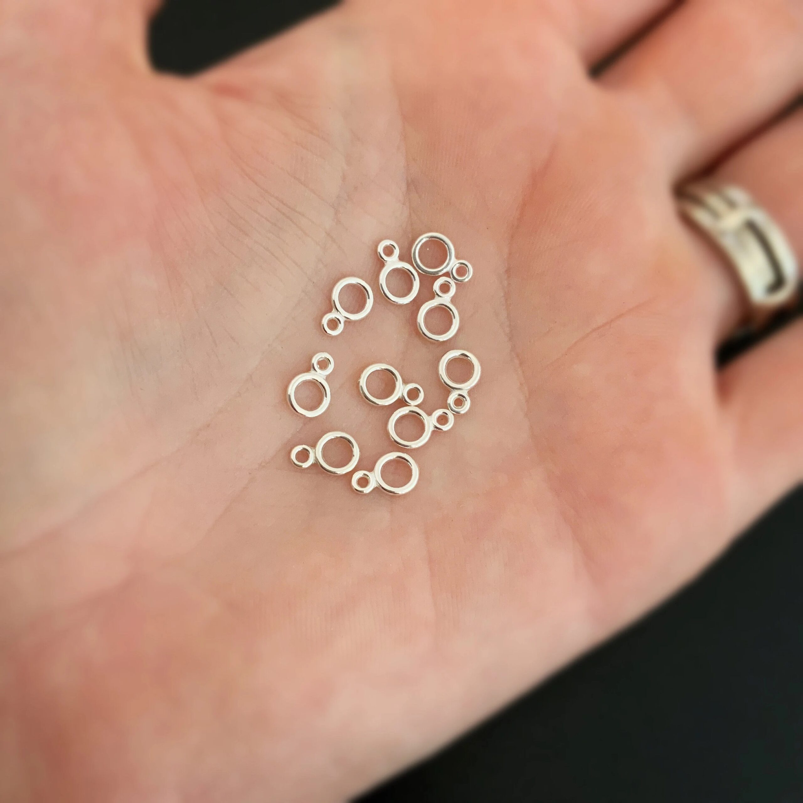 Pile of sterling silver double jump rings that are shiny against the palm of a hand.